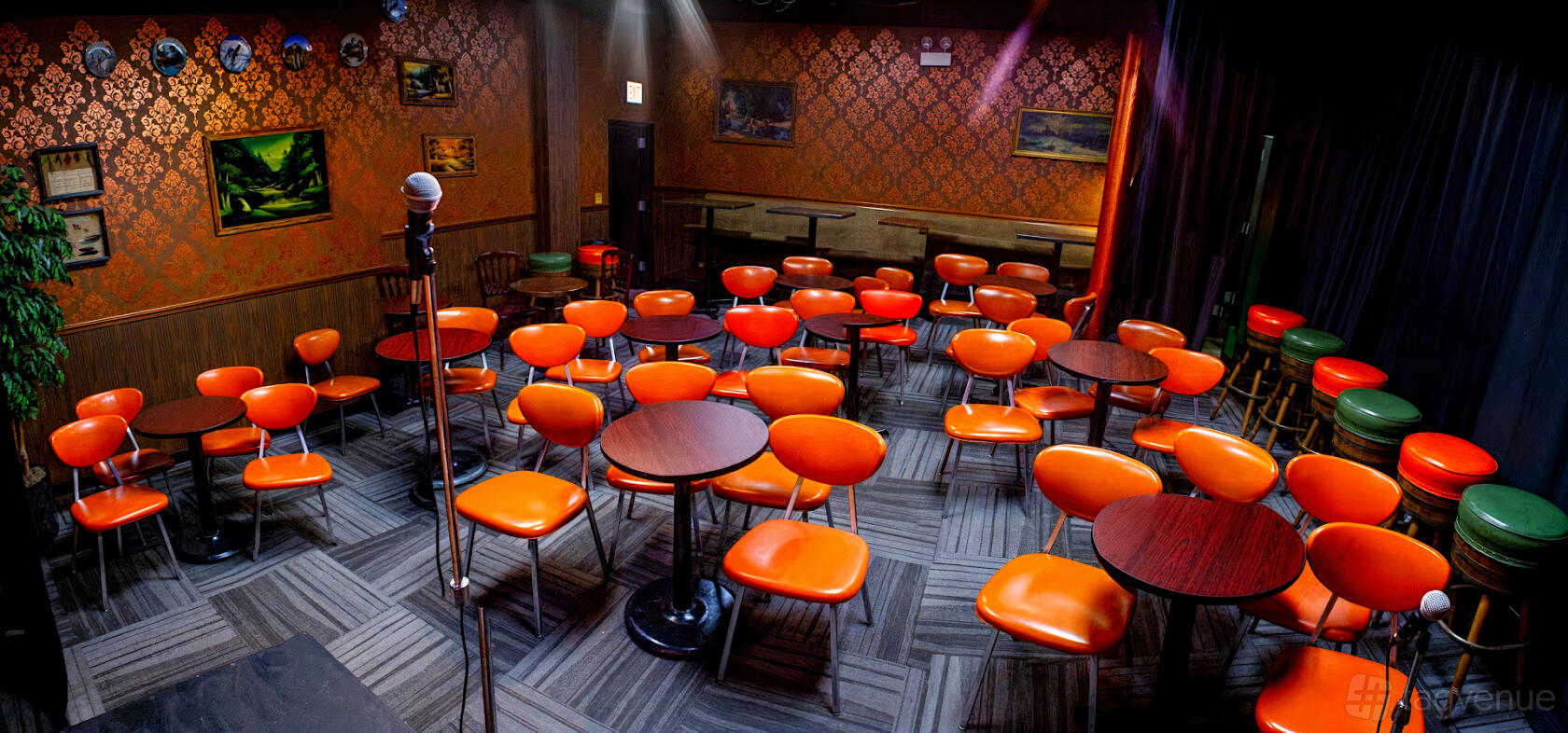 A theatre with orange chairs, round tables, patterned wallpaper, and a microphone on stage at Lincoln Lodge.