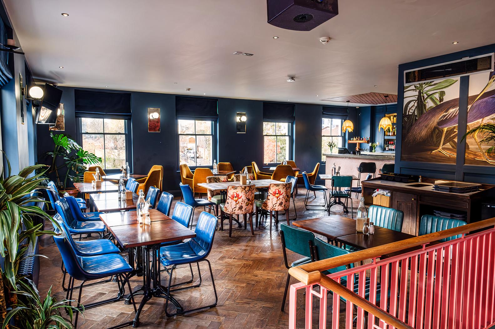 A function room in a pub with dark blue walls, parquet wood floors, eclectic chairs, and natural light at Lord Napier Star.