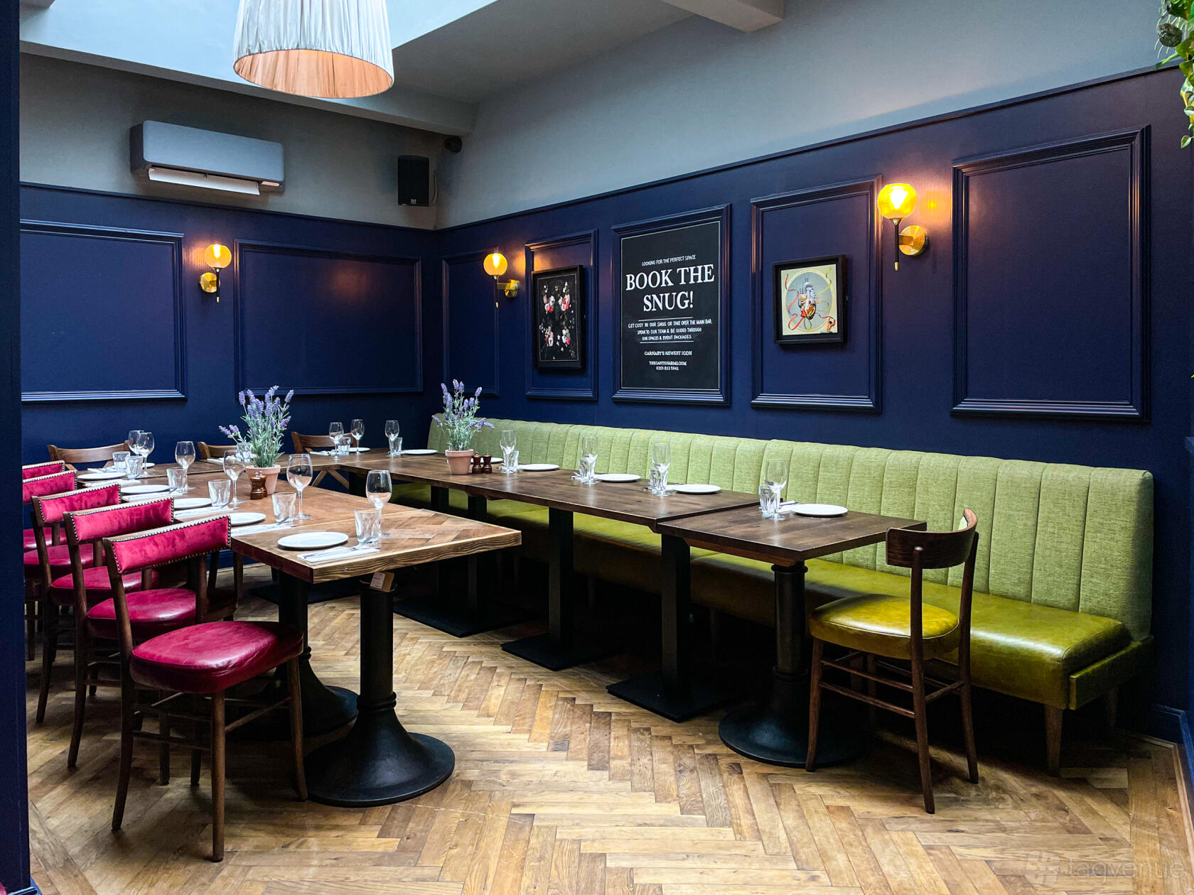 An intimate event space with navy blue paneled walls, wooden tables, and a green upholstered bench at The Ganton Arms.