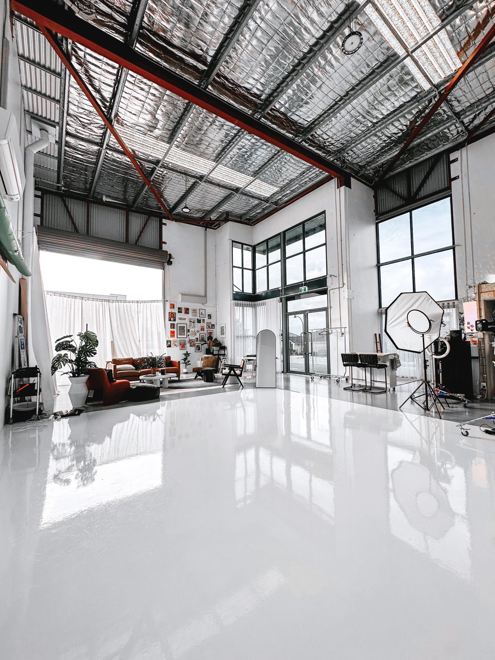 A photo studio with high ceilings, large windows, polished white floors, and studio lighting equipment at Sol Tank Studio.