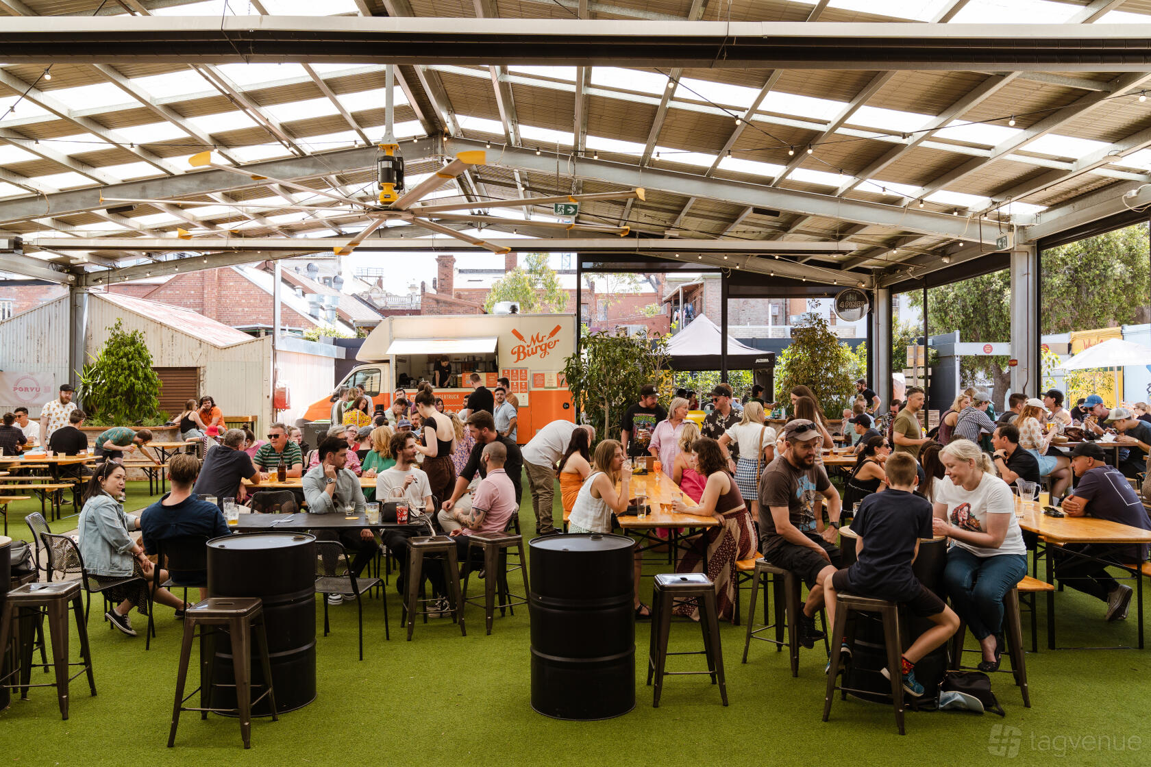 A covered terrace at a winery with artificial turf, communal wooden tables, and greenery at Welcome to Brunswick.