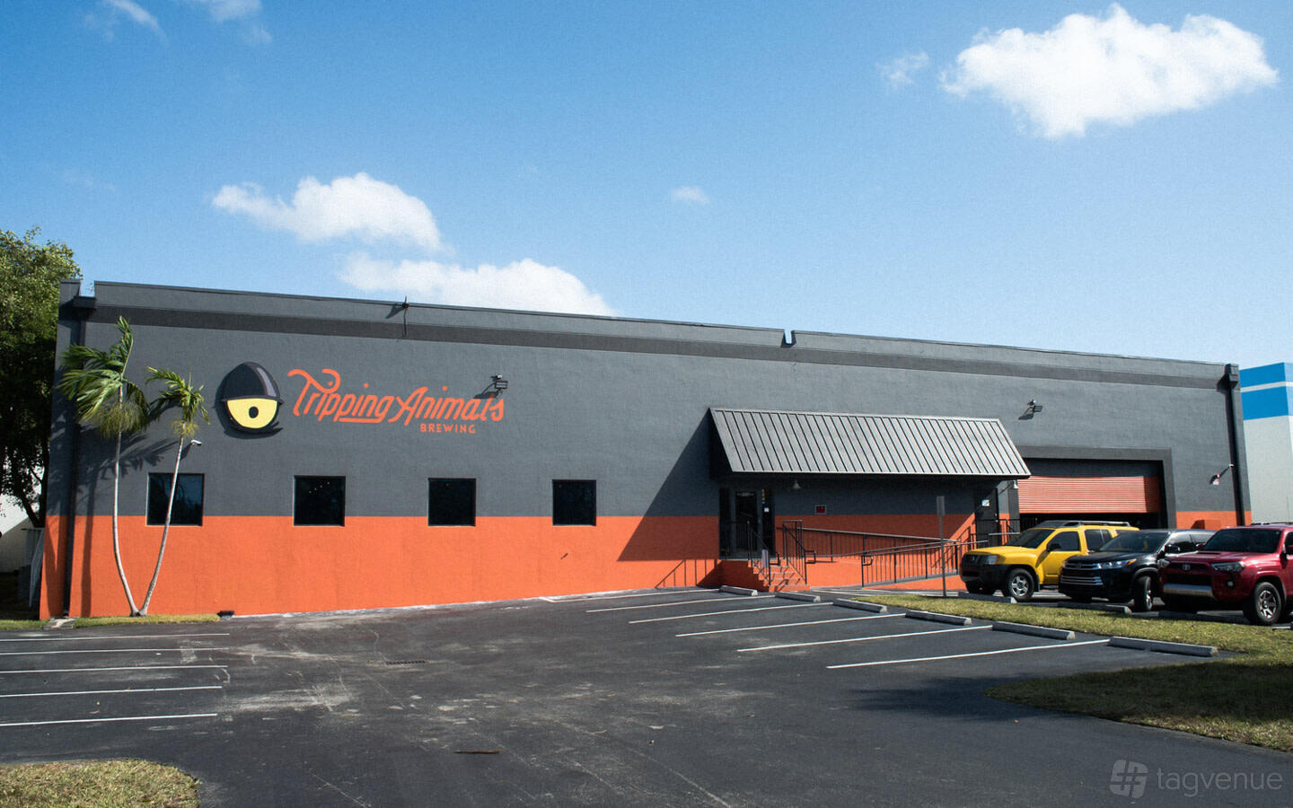 A brewery with a gray and orange facade, metal awning, and parking area at Tripping Animals Brewing Co.