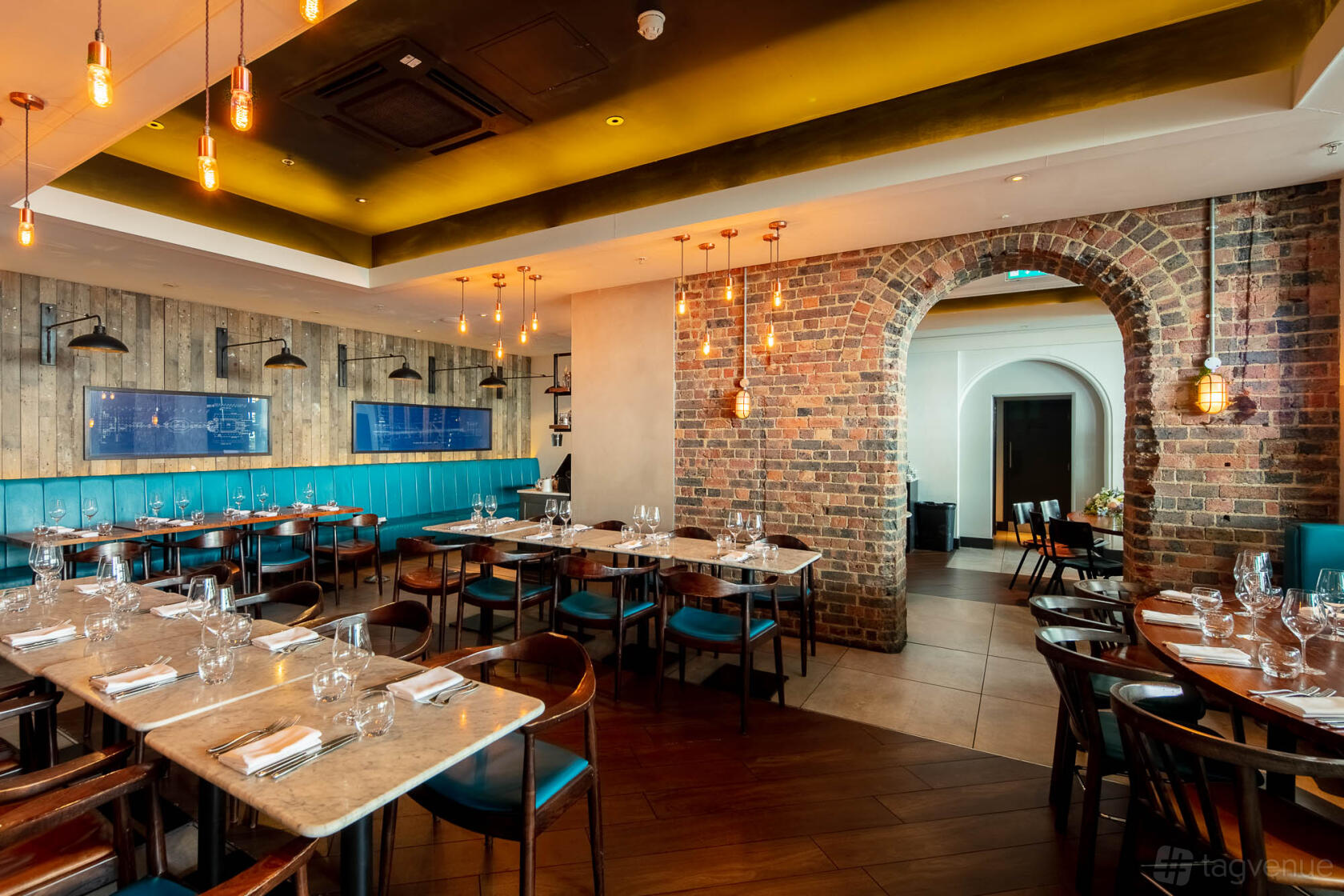 A restaurant with exposed brick archway, pendant lighting, and teal banquette seating at The Salt Room.