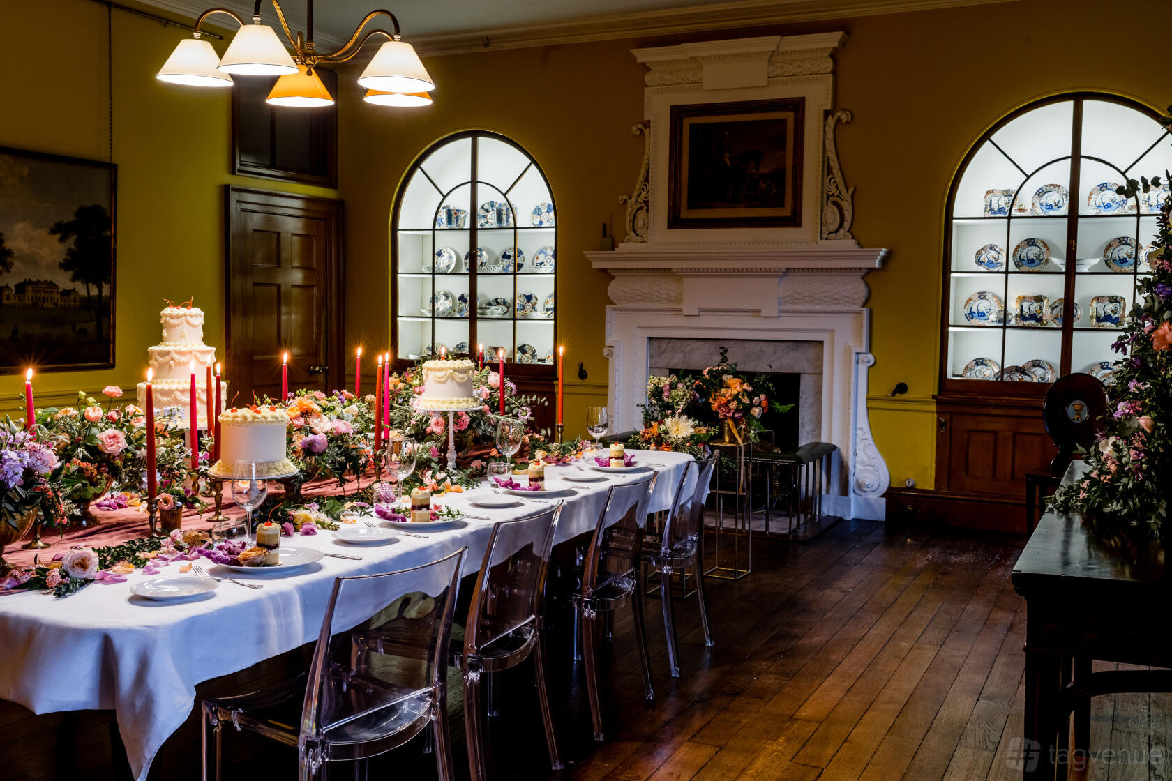 An event space in a country house with a long banquet table, floral centerpieces, and a decorative fireplace at Harewood House.