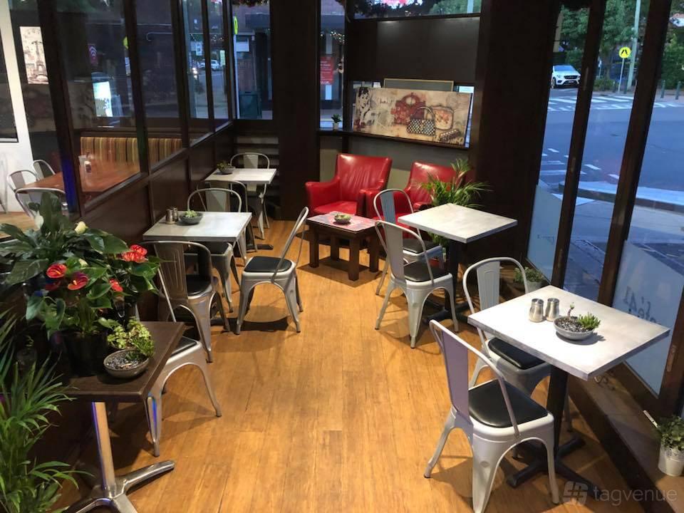 A cafe with wood flooring, metal chairs, potted plants, and a red armchair at Cafe Tabouli.