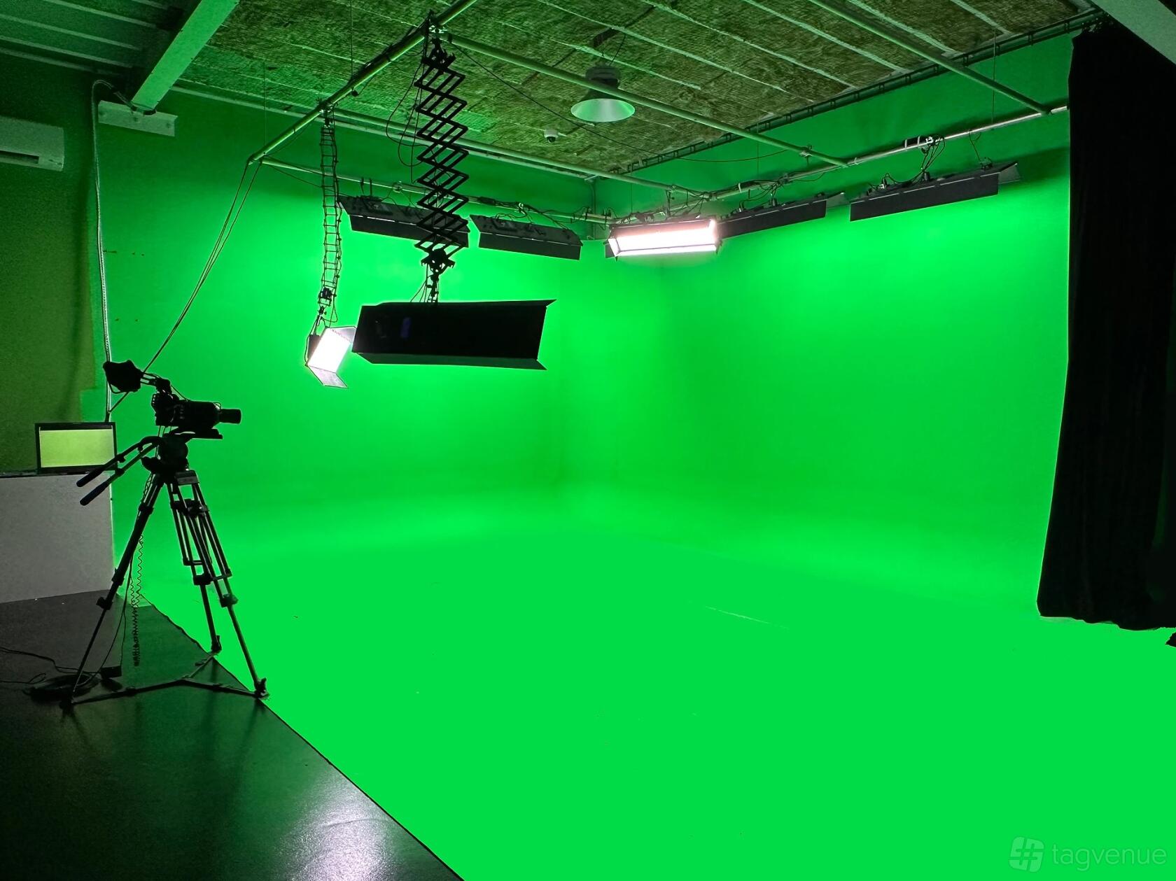 A TV studio with a seamless green screen, ceiling lights, and a camera setup at Damn Good Productions.