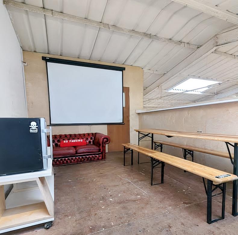 A gallery studio with skylights, a red leather sofa, a projector screen, and wooden benches at School of Skate Copeland Park.