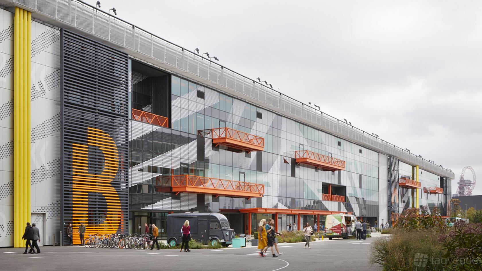 A coworking space with geometric glass facade, orange balconies, and outdoor seating at PLEXAL.