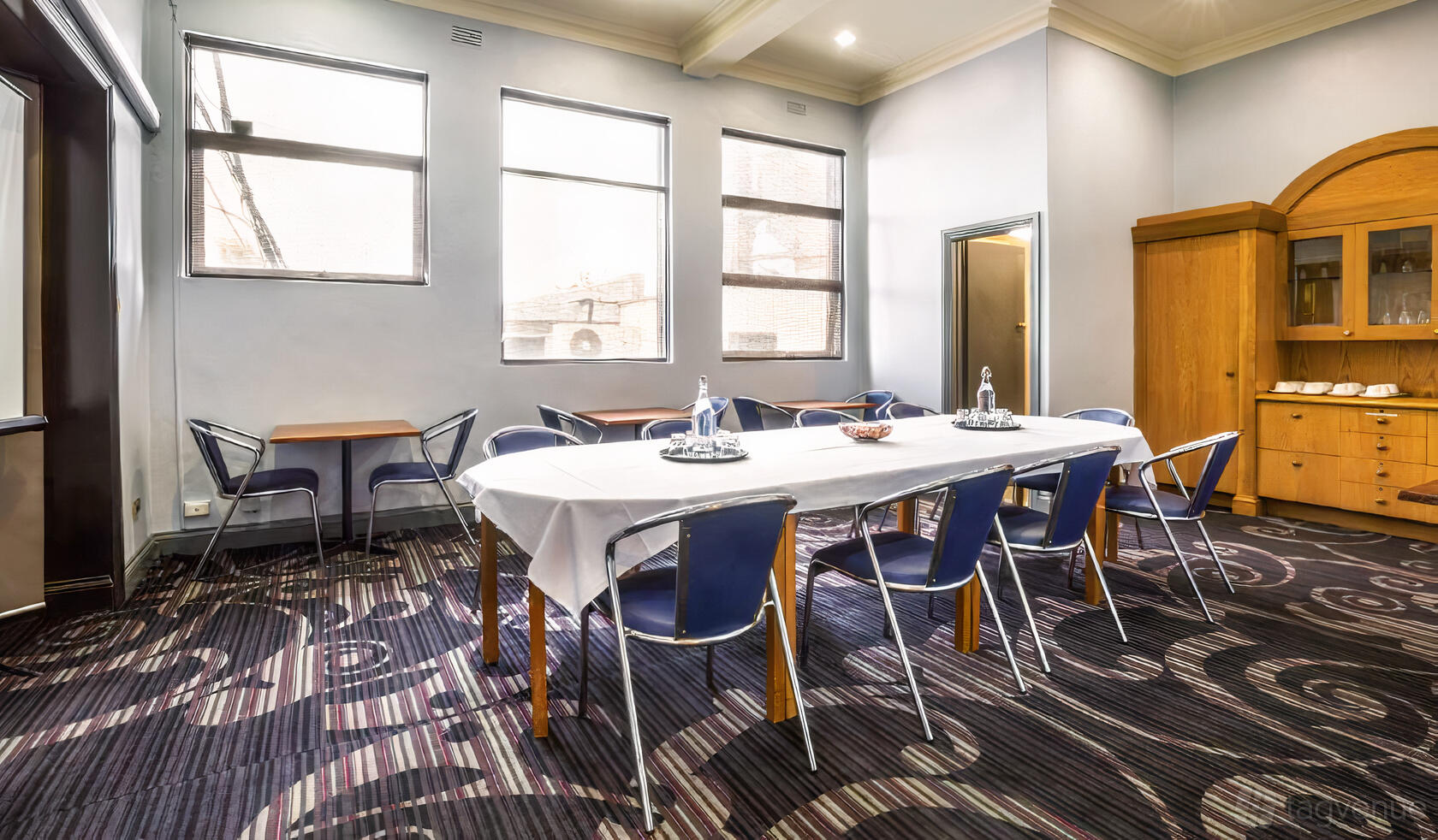 A meeting room with patterned carpet, long table with white linen, and blue chairs at Skyways Hotel.