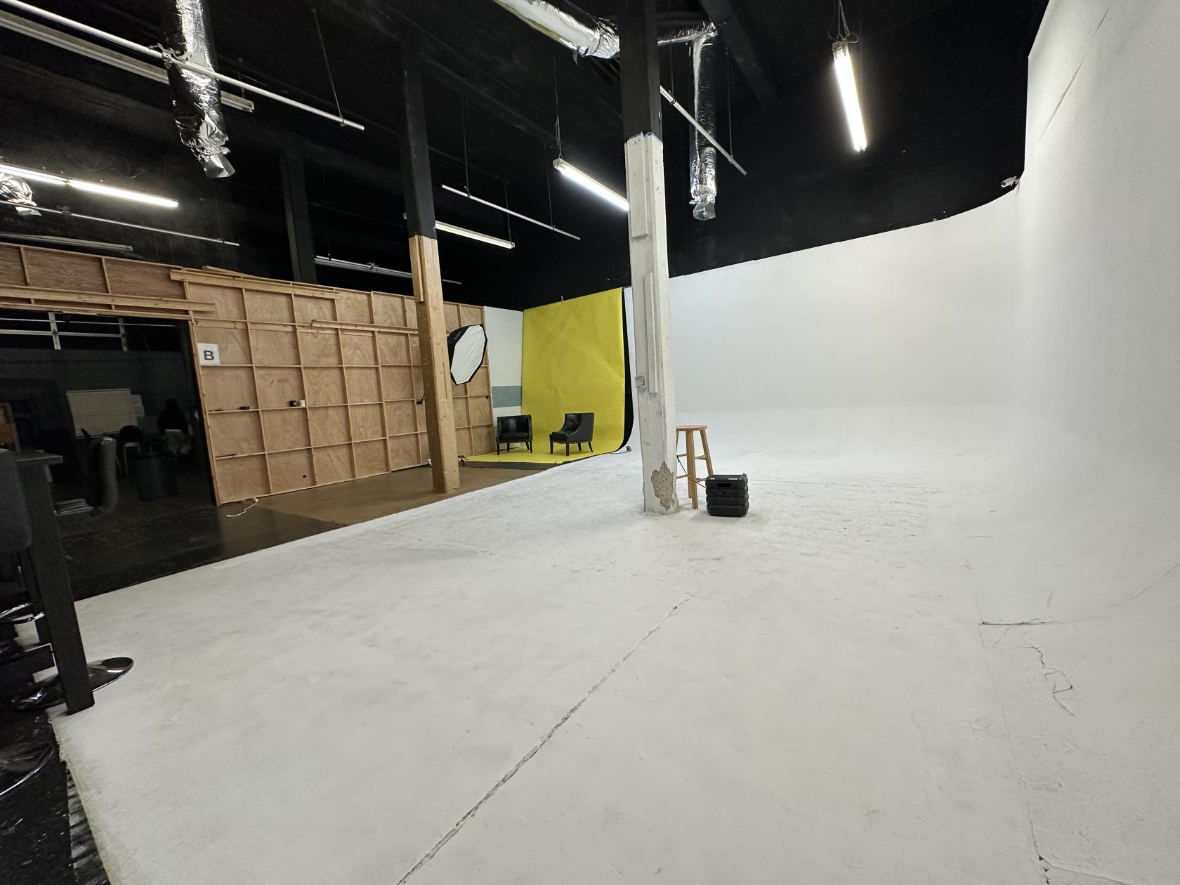 A film studio with a large white cyclorama wall, overhead lighting, and a yellow backdrop at Playback Studios.