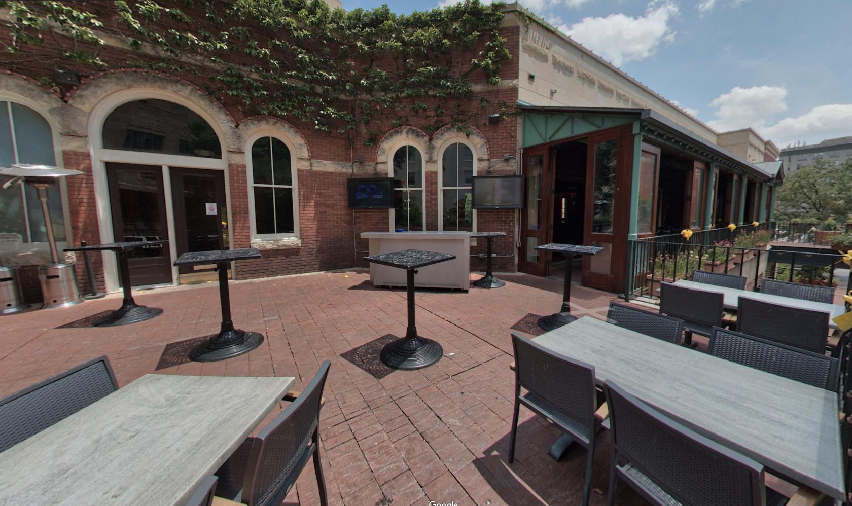 An outdoor event space with brick flooring, high-top tables, and ivy-covered brick walls at Howl at the Moon, San Antonio.