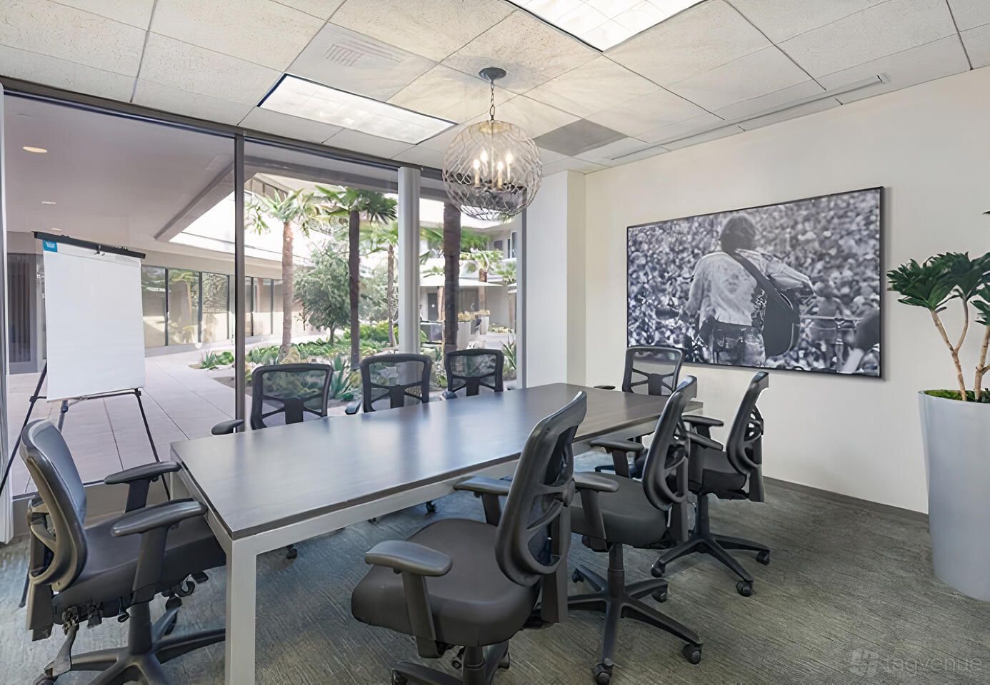 A coworking space with a glass-walled conference room, rolling chairs, and a large wall art at Premier Workspaces - 23 Corporate Plaza.