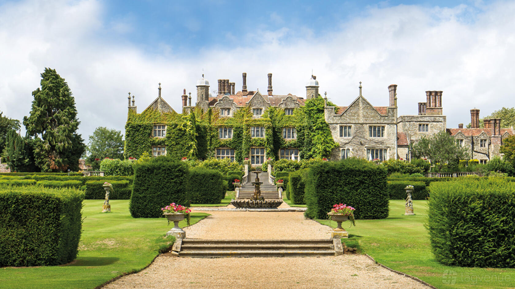 A country house with ivy-covered stone walls, manicured gardens, statues, and a central staircase at Eastwell Manor.