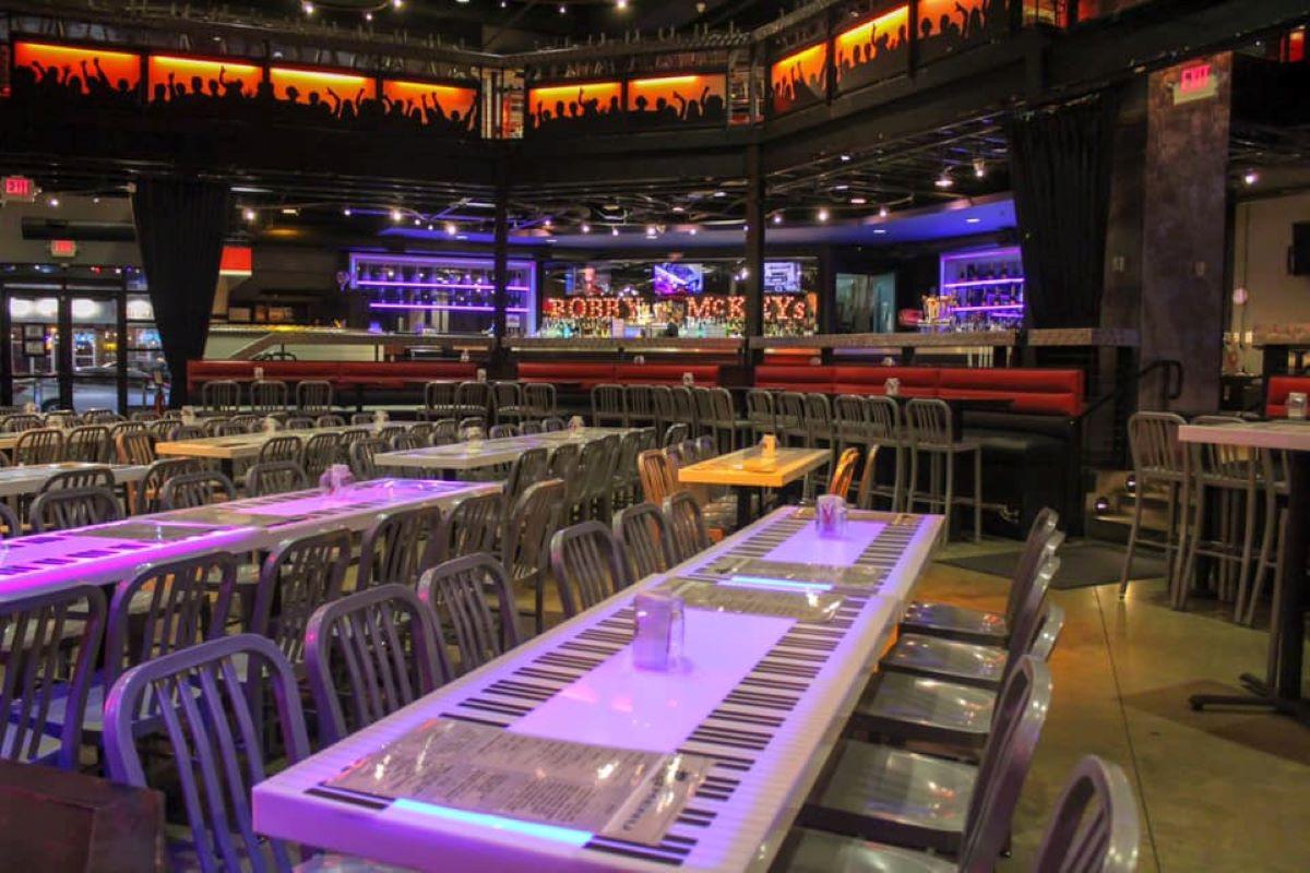 An event space in a bar with piano-themed tables, metal chairs, stage lighting, and a mezzanine at Bobby McKey's Dueling Piano Bar.
