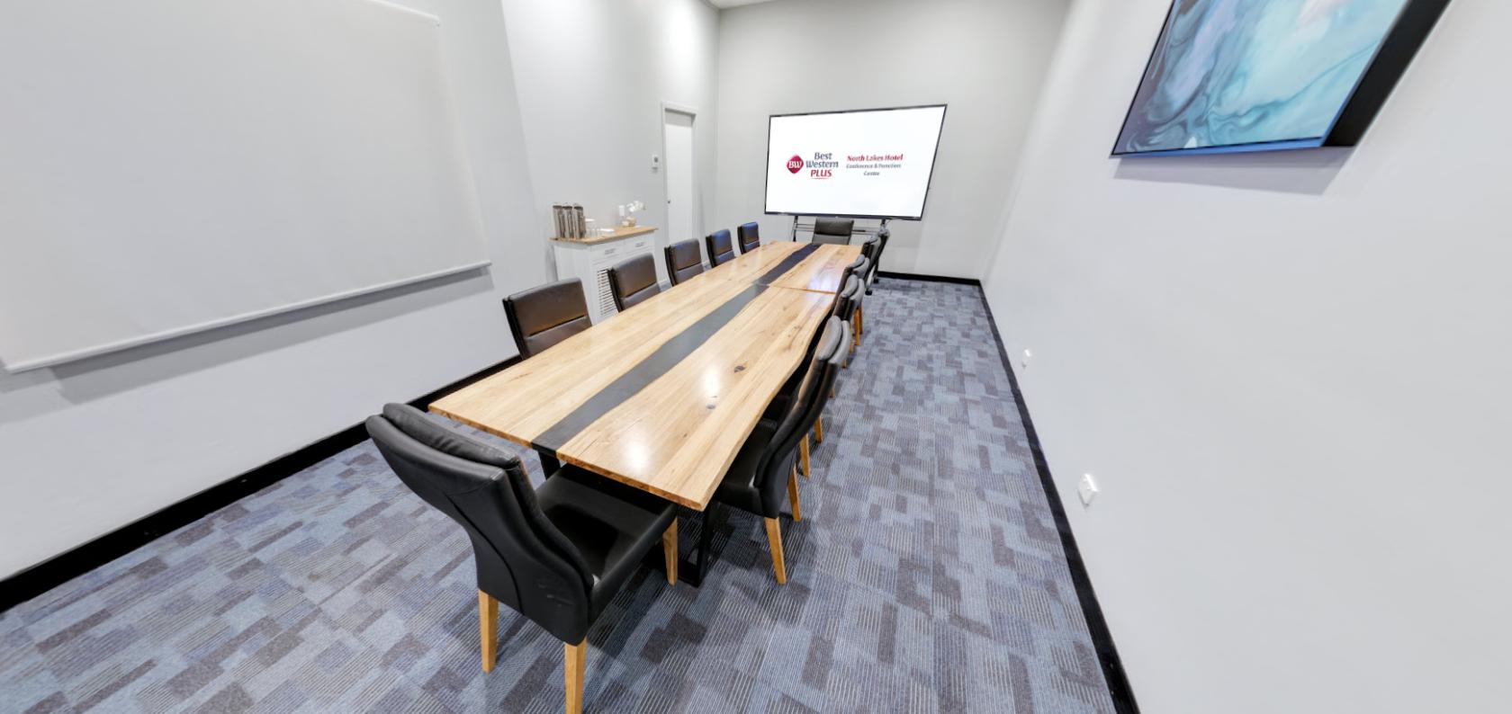 A boardroom with a wooden conference table, leather chairs, and a presentation screen at North Lakes Hotel.