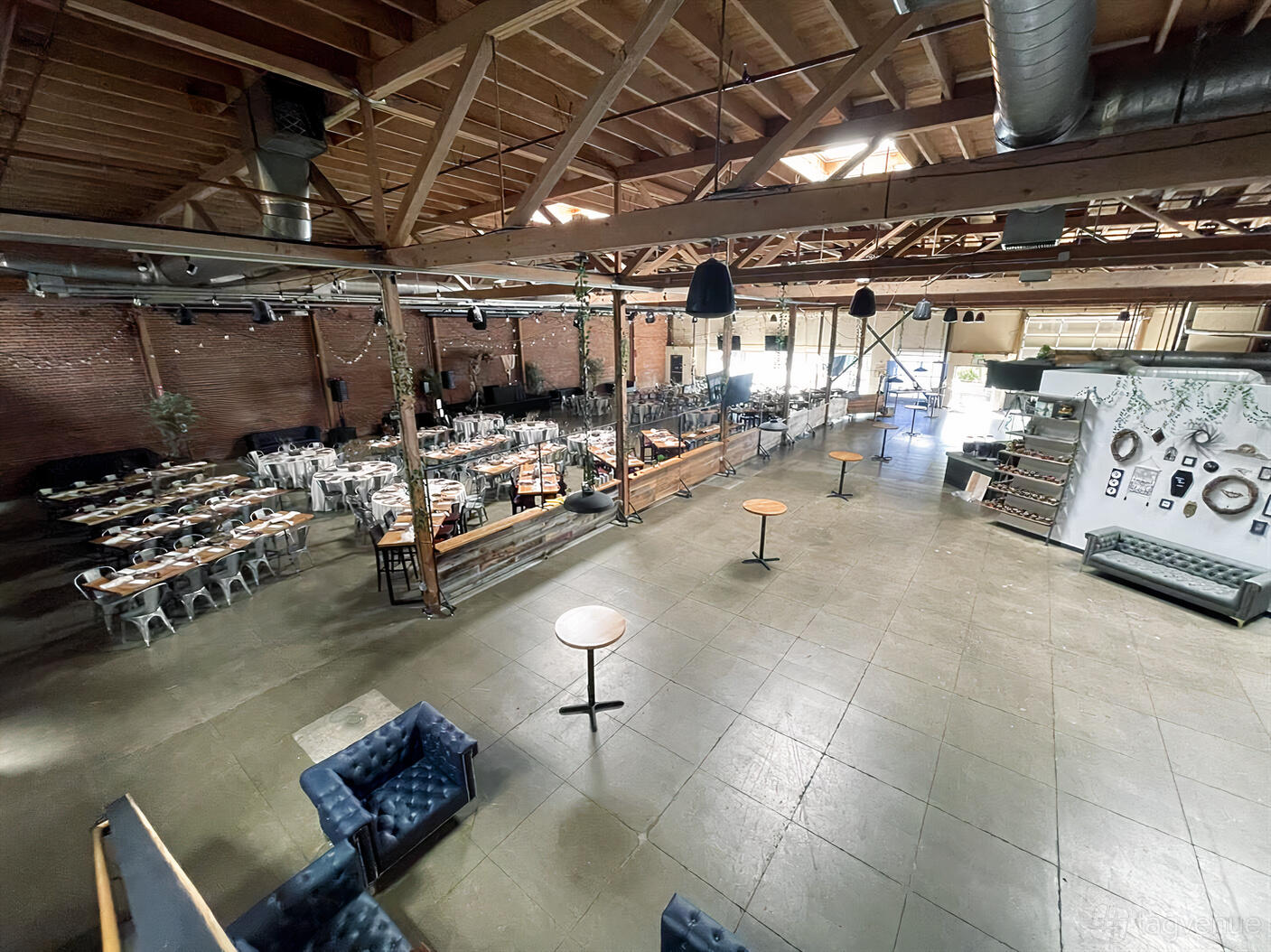 An open bar space with exposed wood beams, brick walls, lounge seating, and banquet tables at Guildhouse.