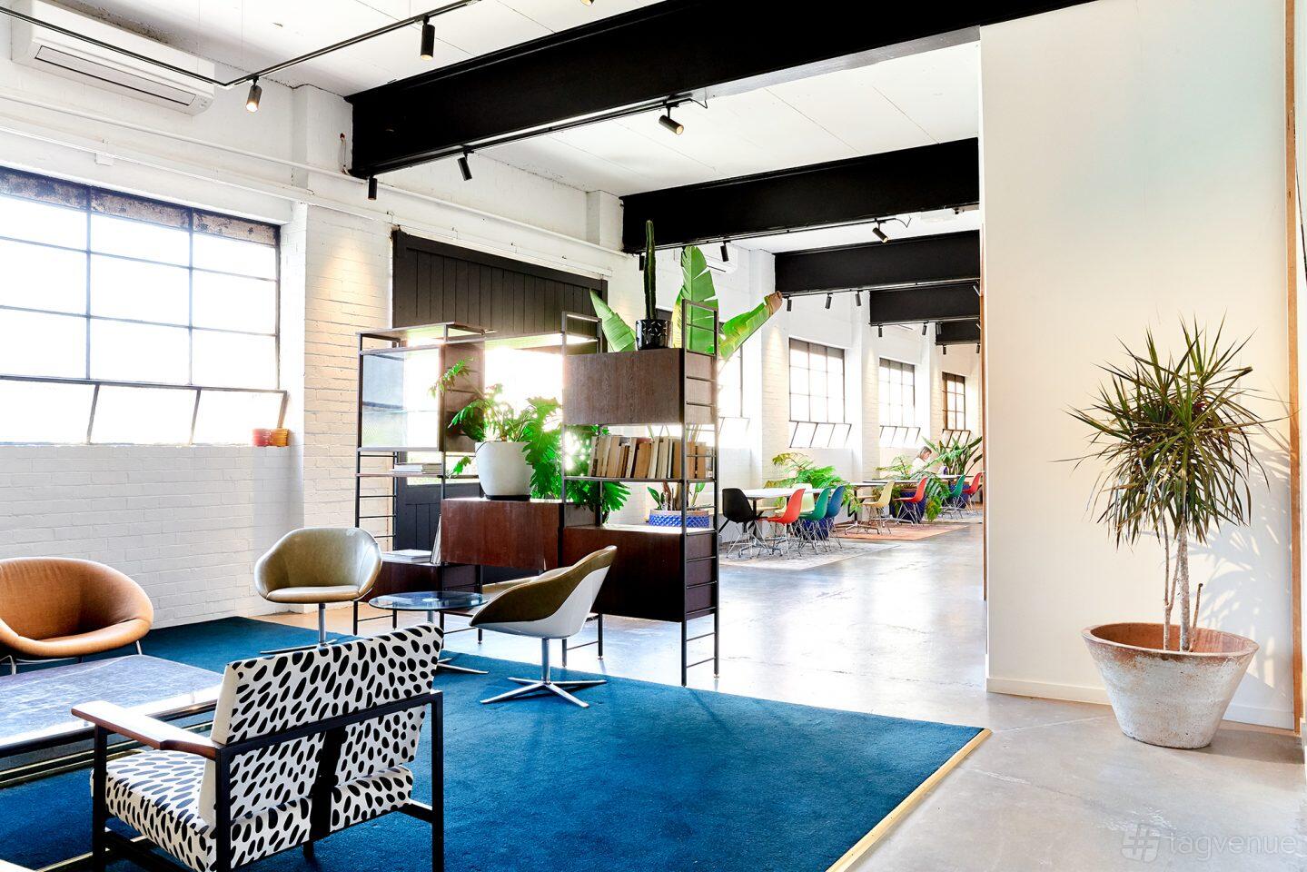 A coworking space with large windows, indoor plants, and contemporary lounge seating at Revolver Lane.
