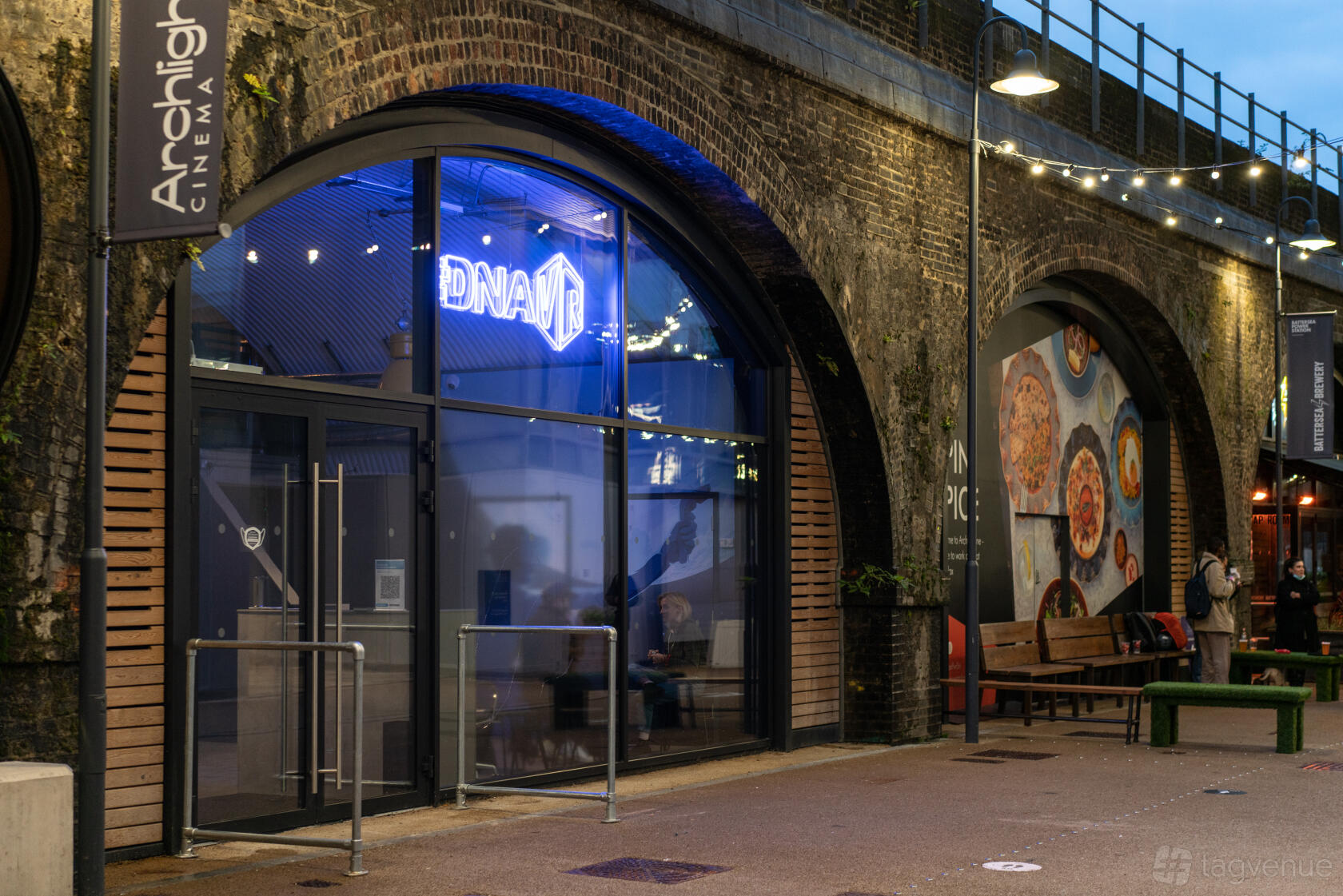 A versatile event space with a glass entrance under brick arches and neon signage at DNA VR Battersea Power Station.