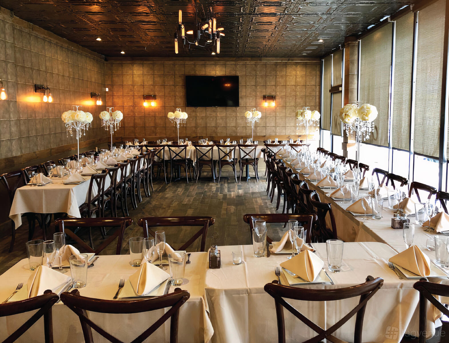 A restaurant dining room with U-shaped tables set with white linens, folded napkins, and crystal centerpieces at Mimmo's Brick Oven Pizza & Trattoria.