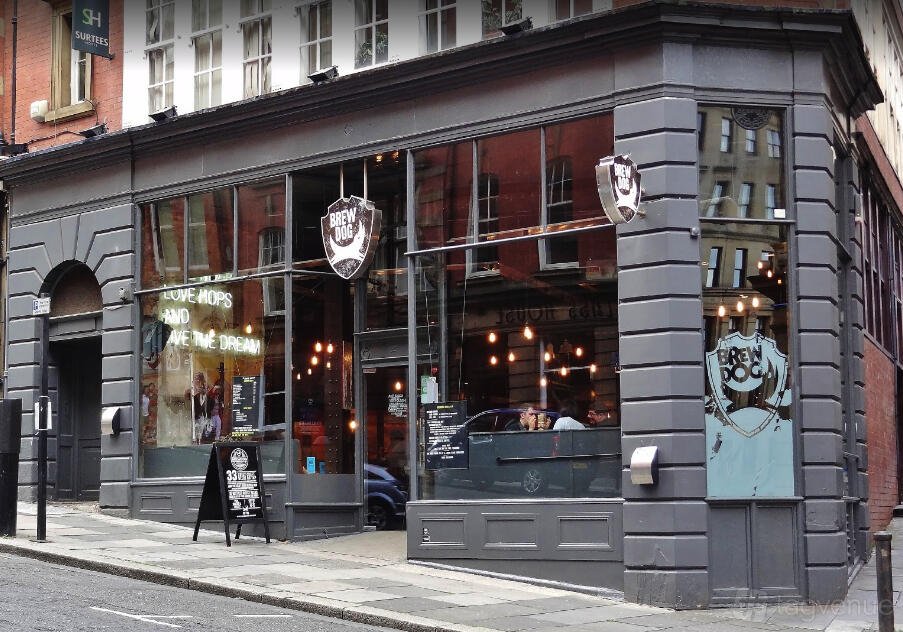 A restaurant with large street-facing windows, grey facade, and hanging pendant lights at BrewDog Newcastle.