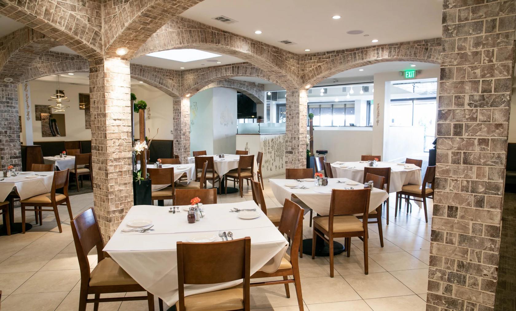 A restaurant with arched stone columns, white tablecloths, and wooden chairs at Sadaf Restaurant Encino.