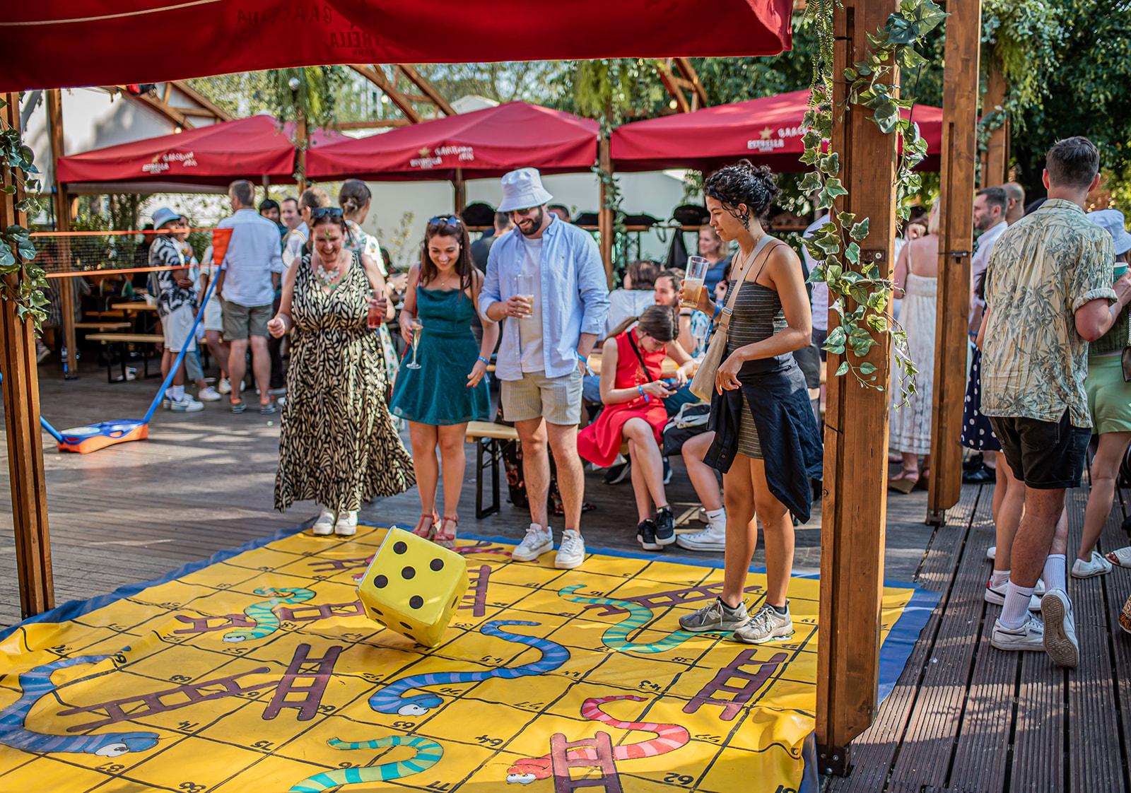 An outdoor event venue with wooden decking, canopy tents, and a life-sized board game at Between the Bridges.