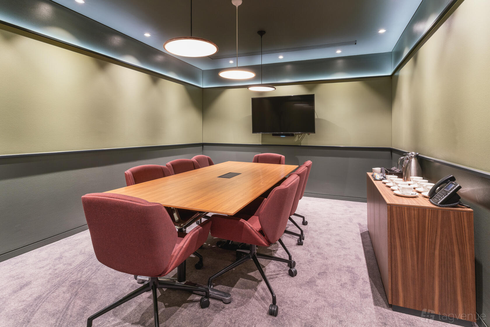 A meeting room with a long wooden table, red chairs, wall-mounted screen, and drinks station at 1 Cornhill.