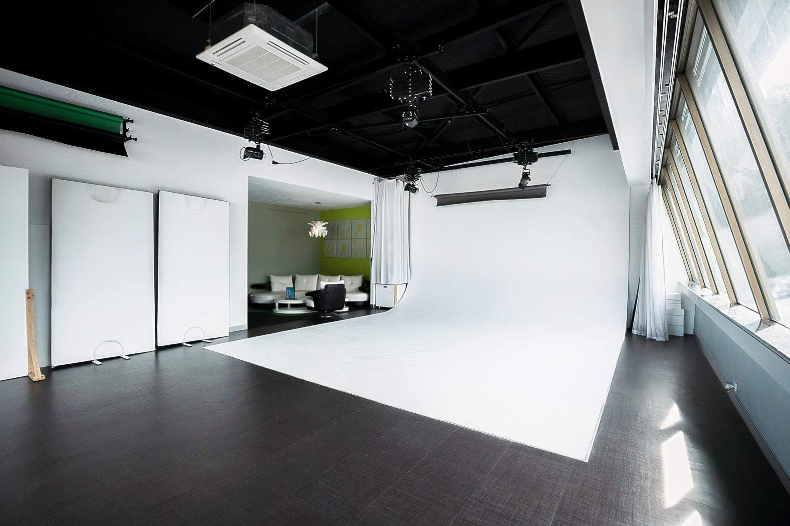 A photo studio with a large white cyclorama wall, dark flooring, and floor-to-ceiling windows at Studio Northbridge.