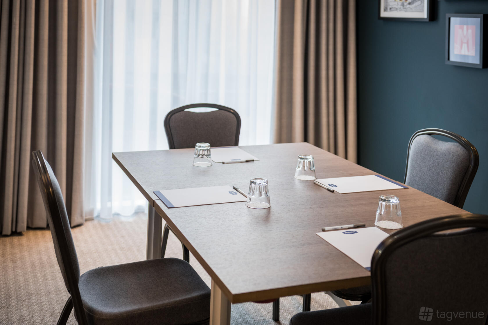A hotel meeting room with a rectangular table, notepads, glasses, and natural light at Hampton by Hilton Manchester Northern Quarter.