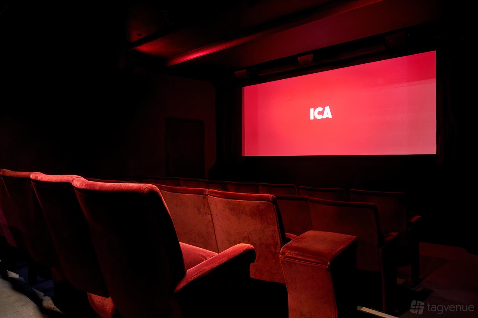A dark cinema with red velvet seats facing a large screen displaying 'ICA' at Institute of Contemporary Arts.