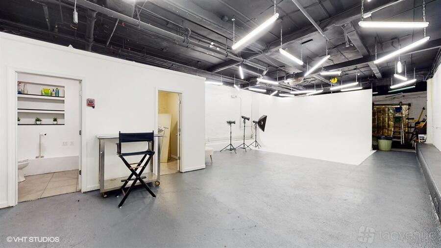 A photo studio with a large white cyclorama wall, lighting equipment, and exposed ceiling at House of Brooklyn.