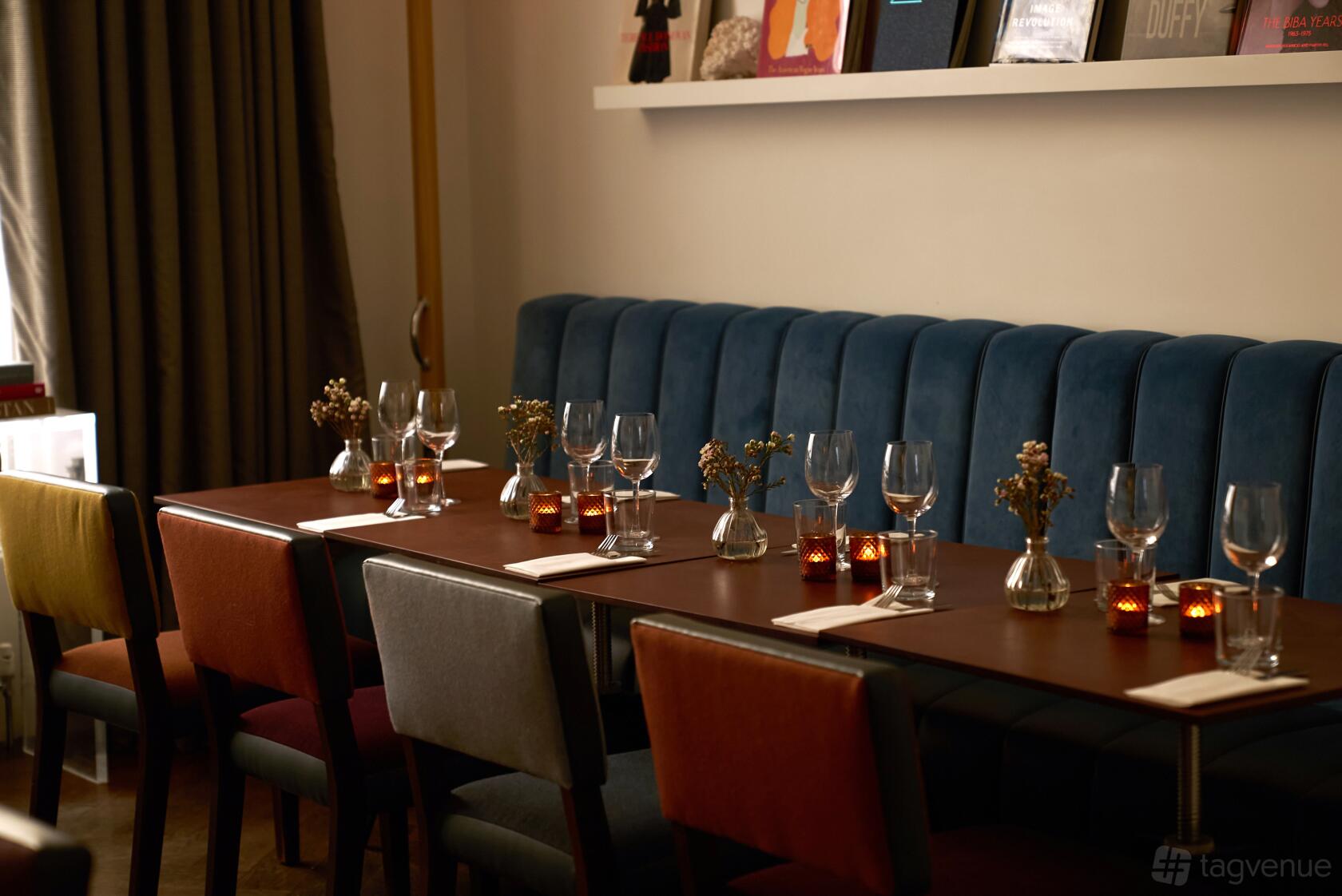 A dining room with a blue upholstered banquette, wooden tables set with glassware, and candlelight at The Laslett.