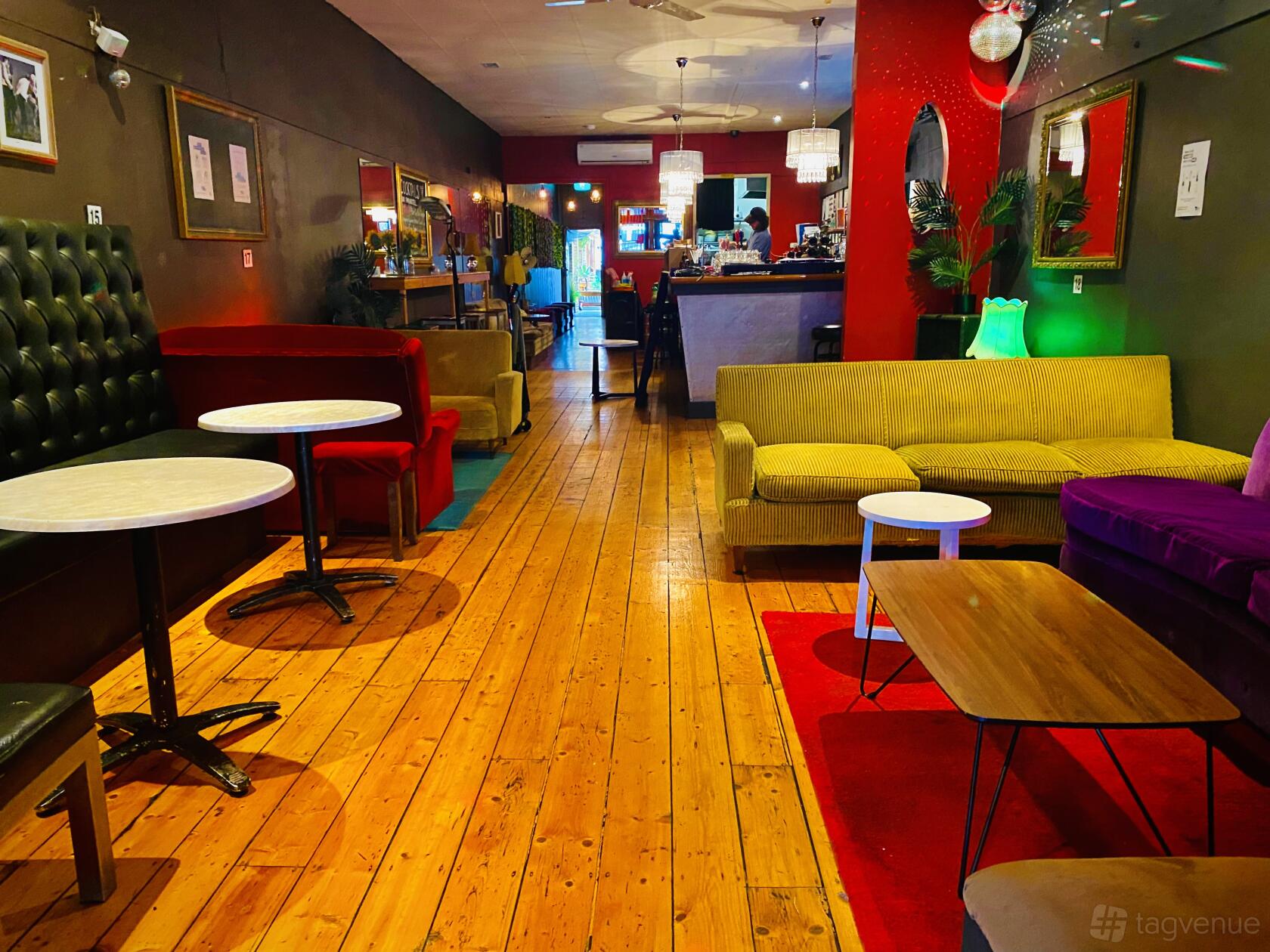 A bar with velvet couches, wooden floors, round tables, and pendant lighting at The Purple Emerald Lounge Bar.