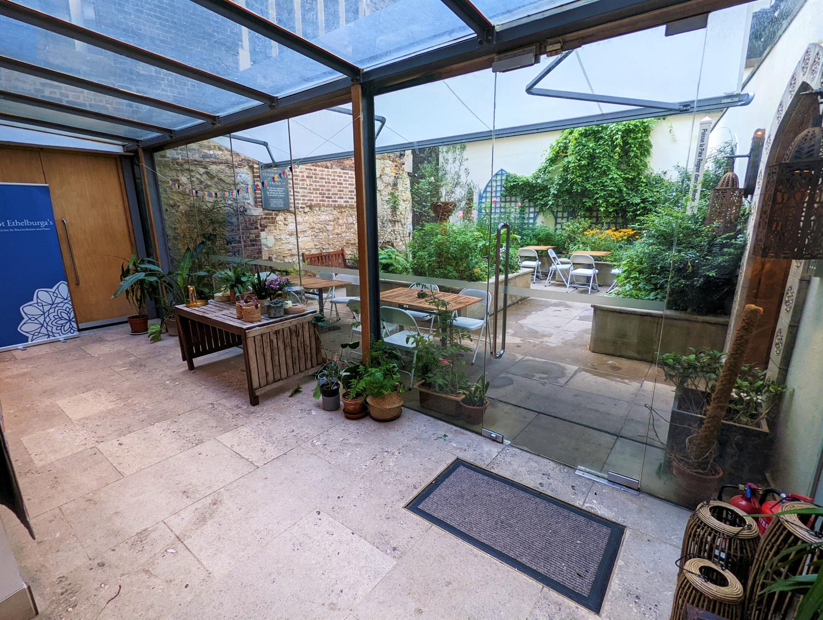 An outdoor church space with potted plants, a covered patio, and garden seating at St Ethelburga's Centre.