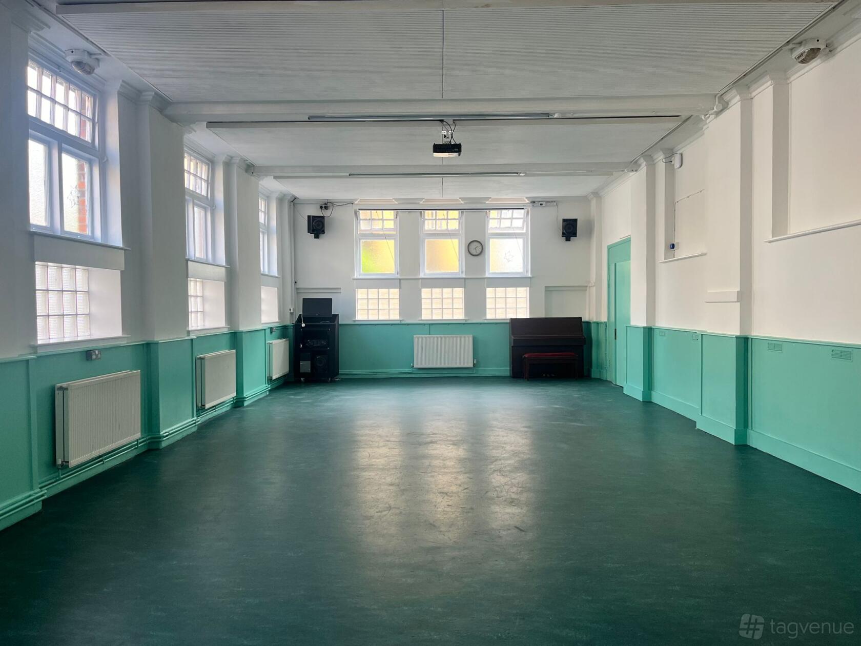 An event space with large windows, teal lower walls, and a polished floor at Katherine Low Settlement.