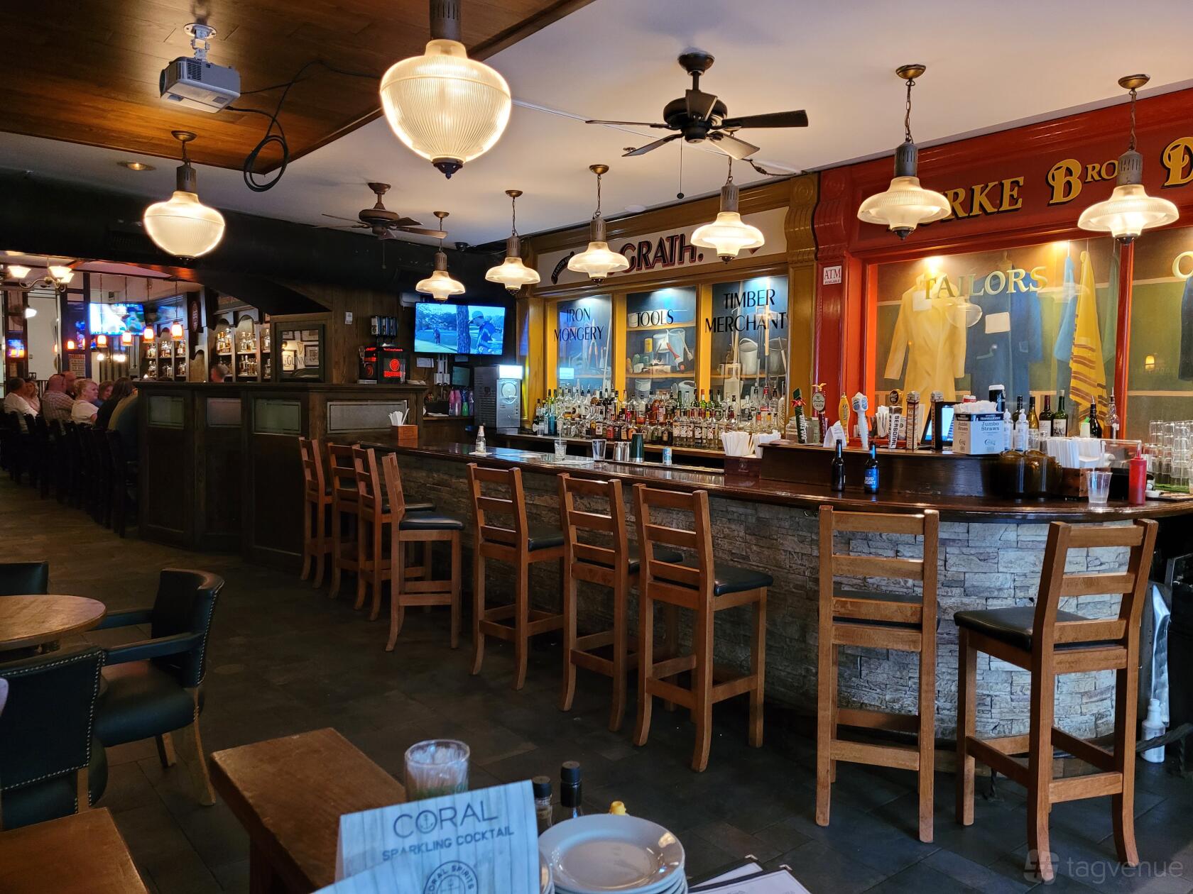 A bar with a long wooden counter, high chairs, hanging pendant lamps, and mirrored back wall at Waxy O'Connors.