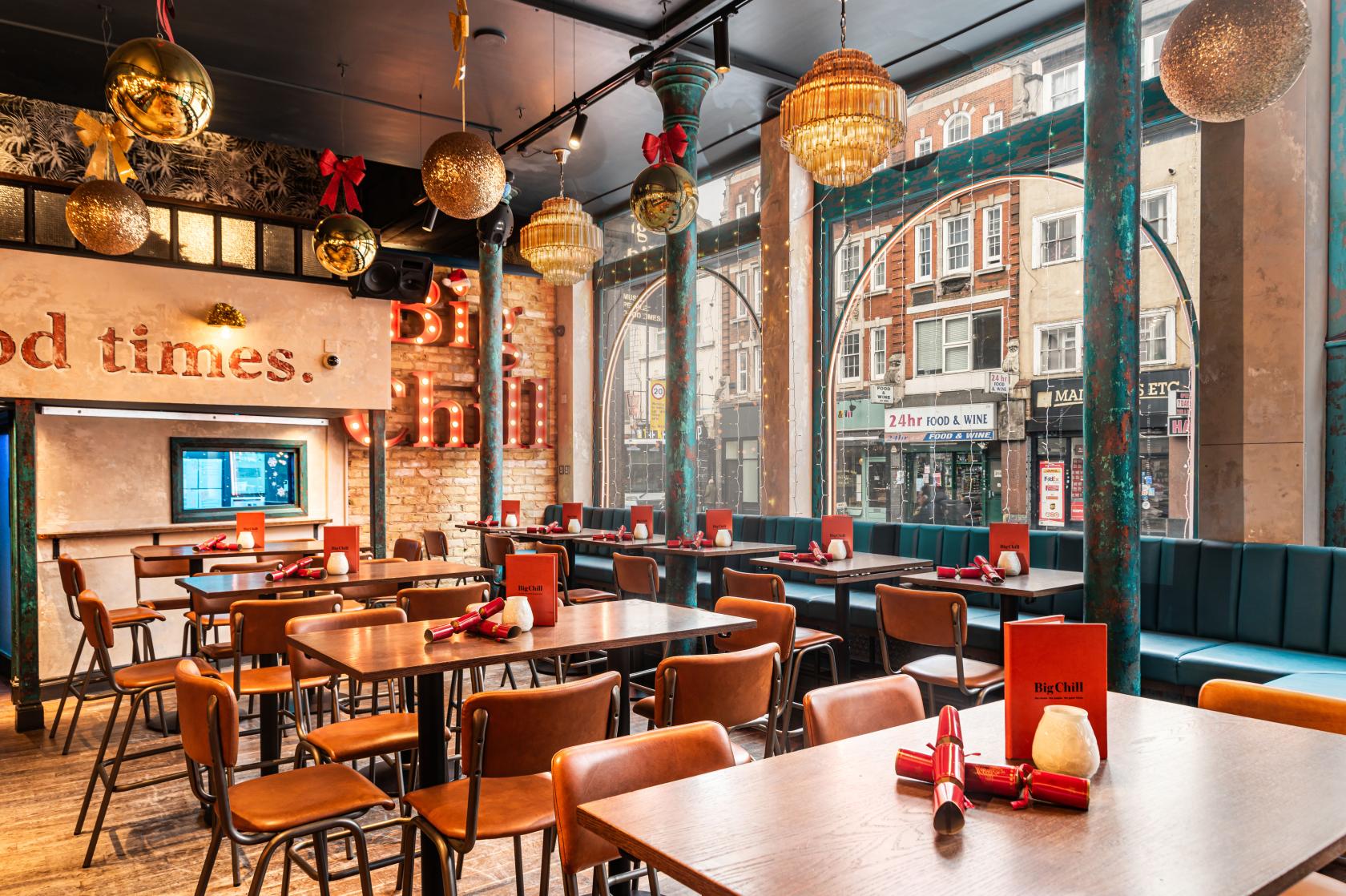 A bar with floor-to-ceiling arched windows, hanging globe lights, brick walls, and wood tables at Big Chill Kings Cross.