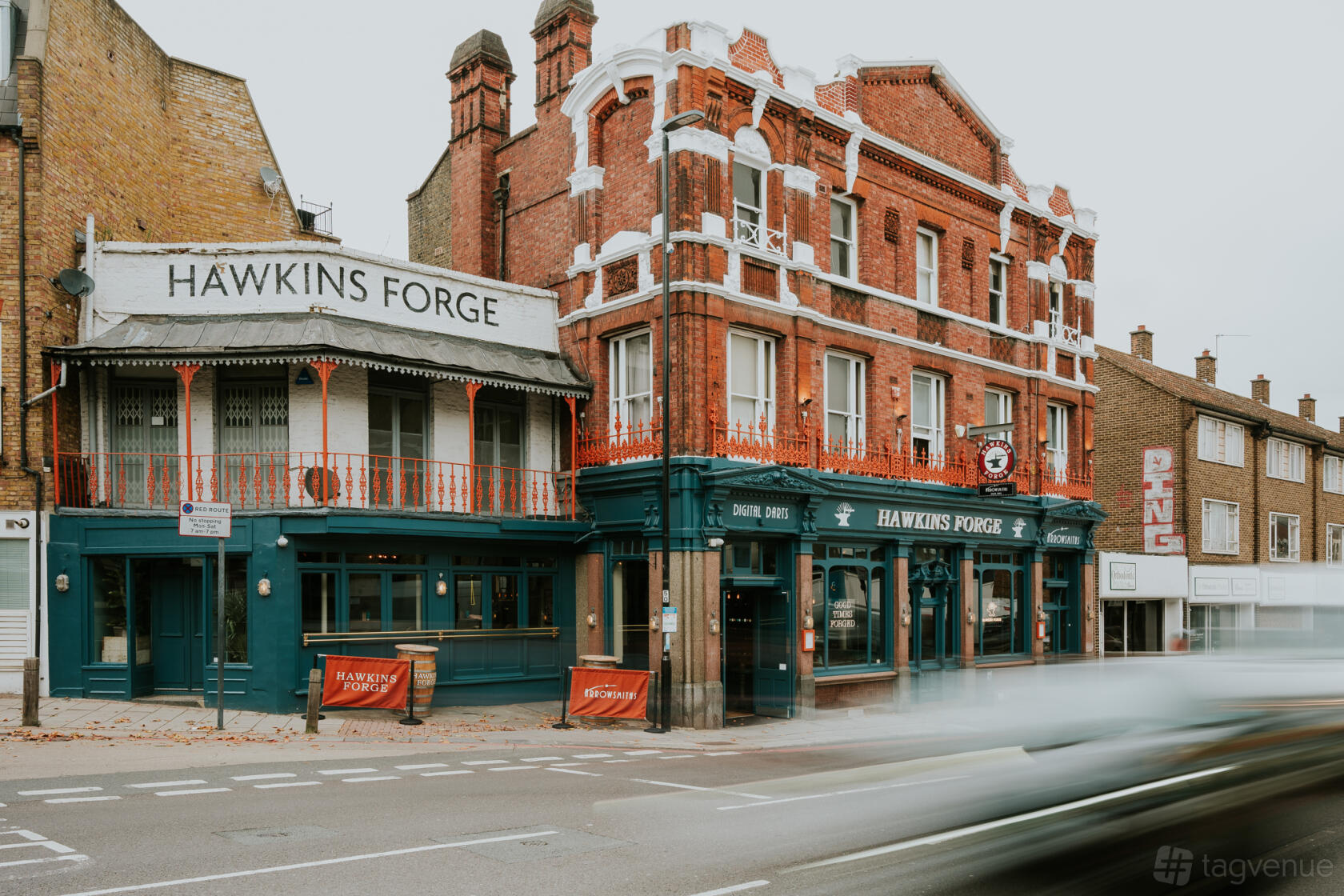 A corner pub with a red brick exterior, decorative balconies, and large front windows at Hawkins Forge.