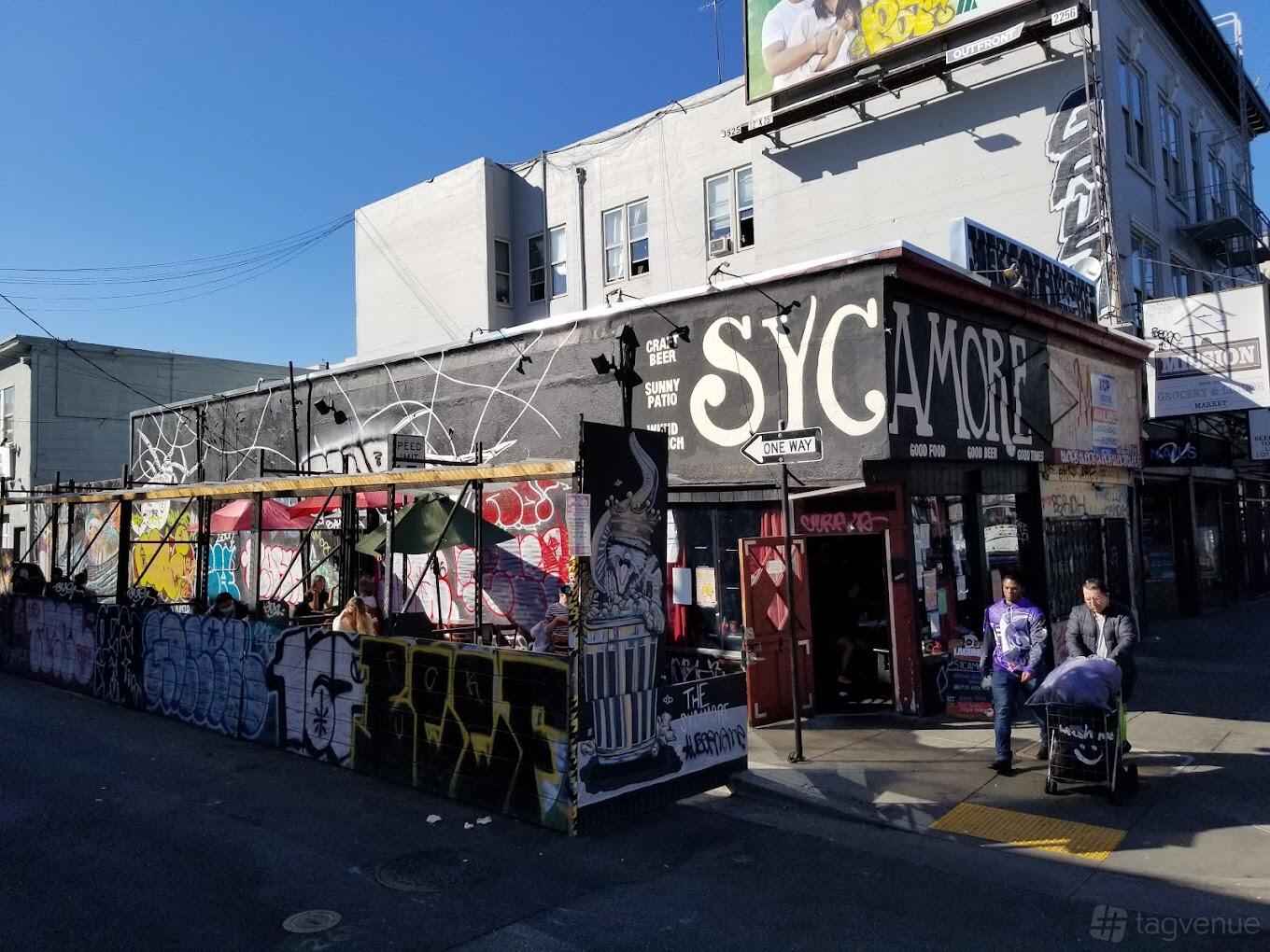 A graffiti-covered bar exterior with a street-side patio and wall mural at The Sycamore.