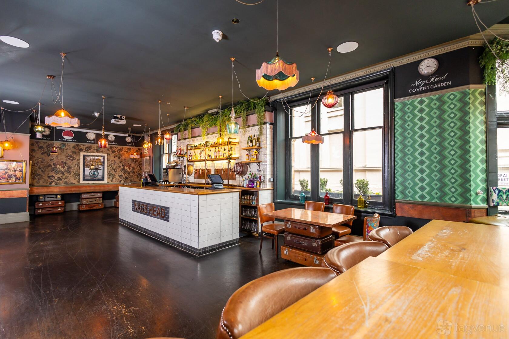A pub dining room with vintage pendant lights, a tiled bar, and large windows at Nags Head, Covent Garden.