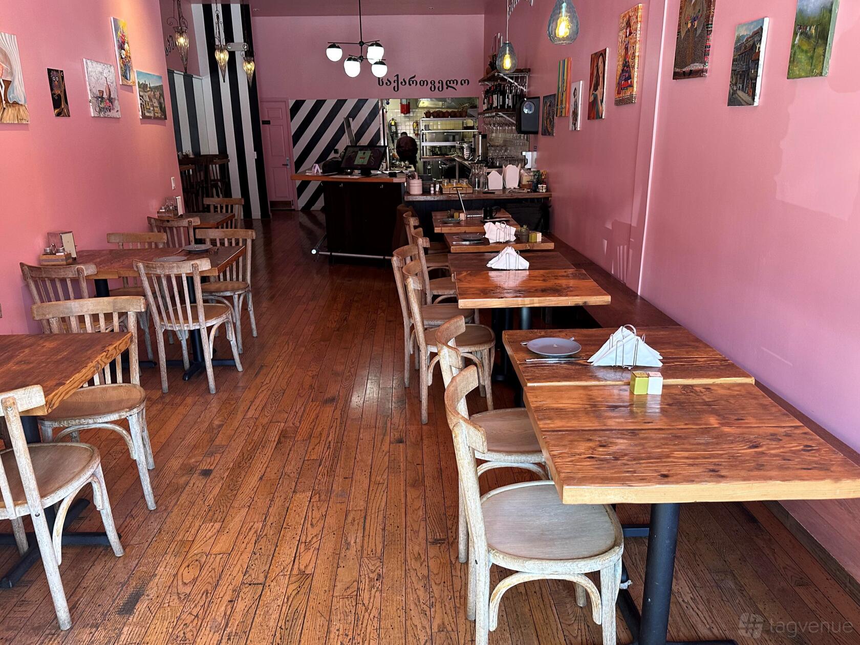 A restaurant with wooden floors, rustic wooden tables, and pink walls at Georgian Cheese Boat.