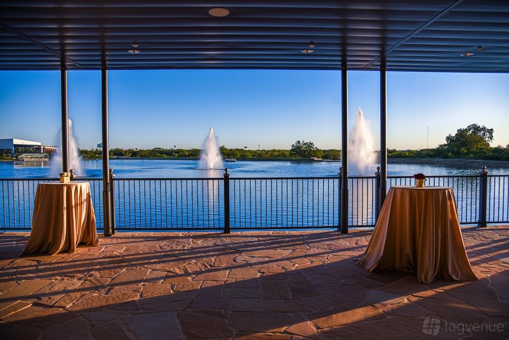 An event venue with a covered terrace, stone flooring, and views of fountains on the lake at The Red Berry Estate.