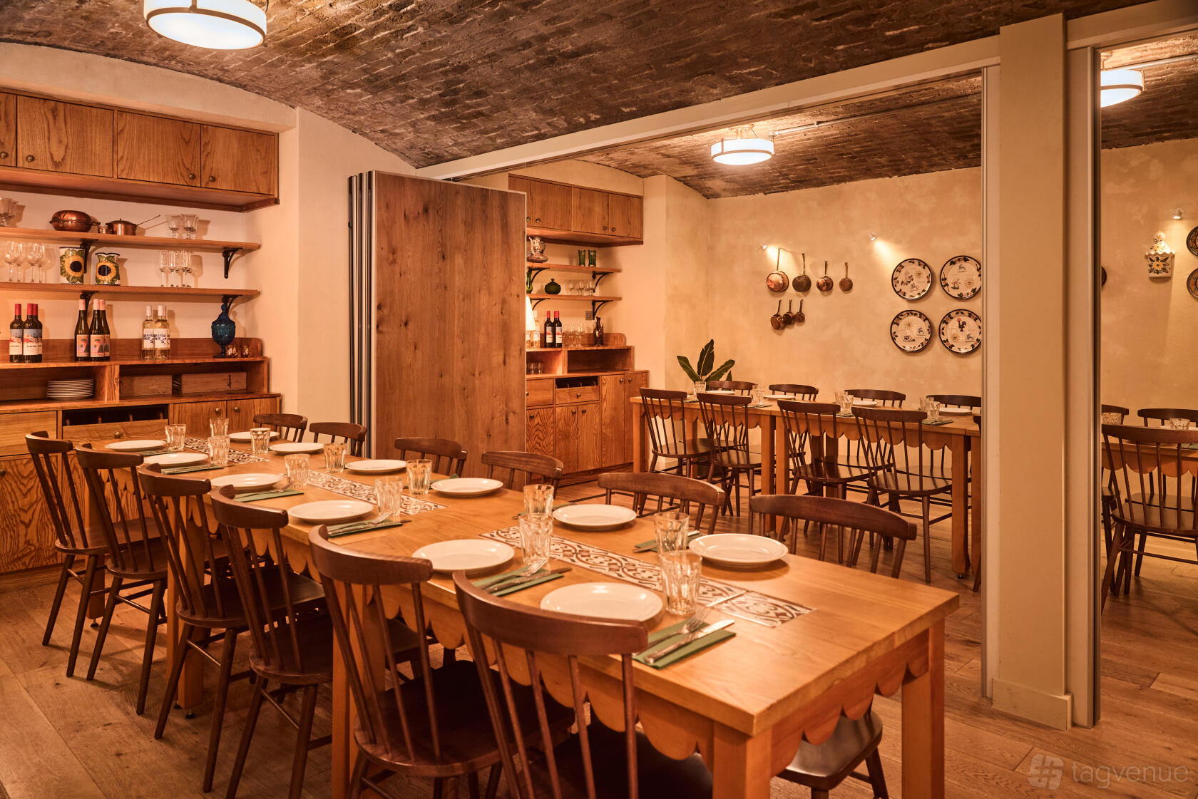 A dining room with long wooden tables, wooden chairs, exposed brick ceiling, and decorative plates at Casa do Frango - Mayfair.