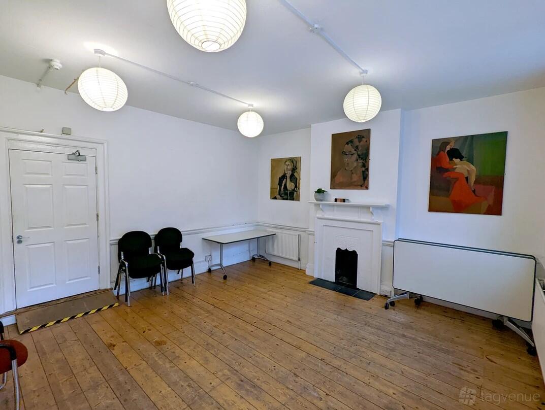 A rehearsal studio with wooden floors, white walls, round paper lantern lights, and artwork at Theatro Technis.