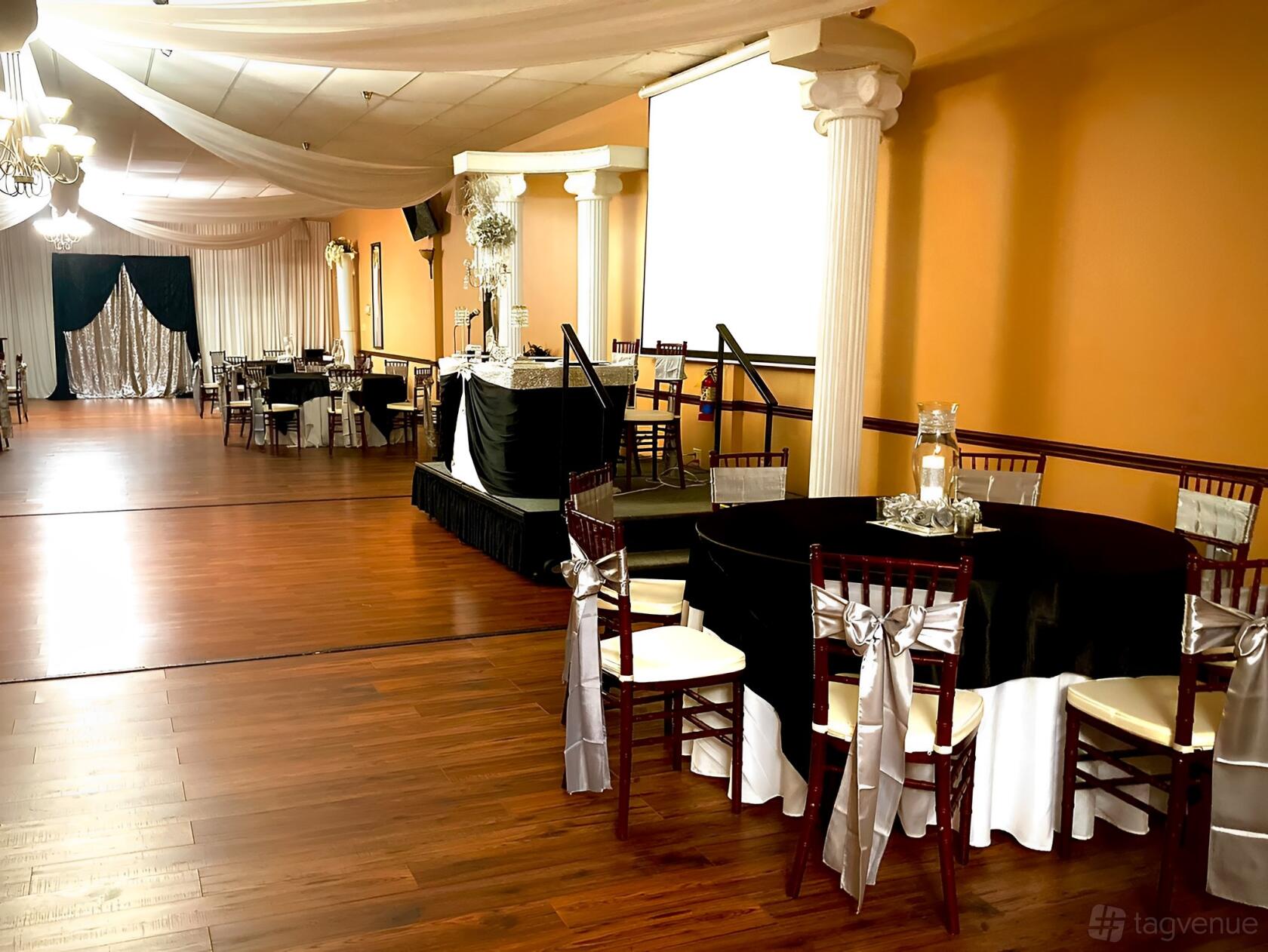 An event venue with wood floors, round tables draped in black linens, and white columns at JS Venue Plus.