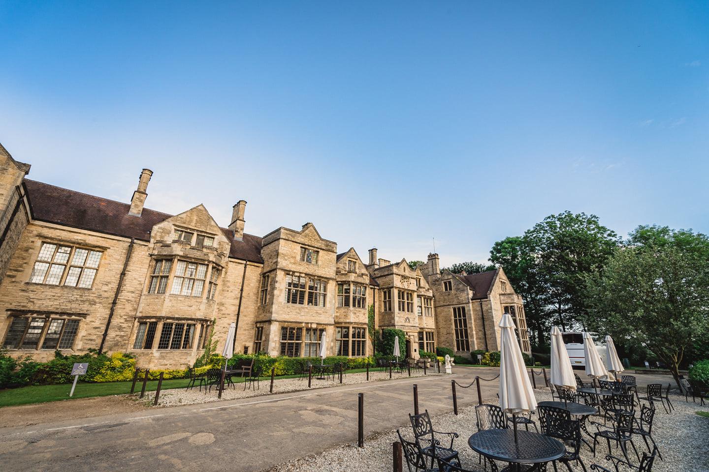 A hotel with historic stone architecture, outdoor seating with metal tables, and parasols at Redworth Hall Hotel.