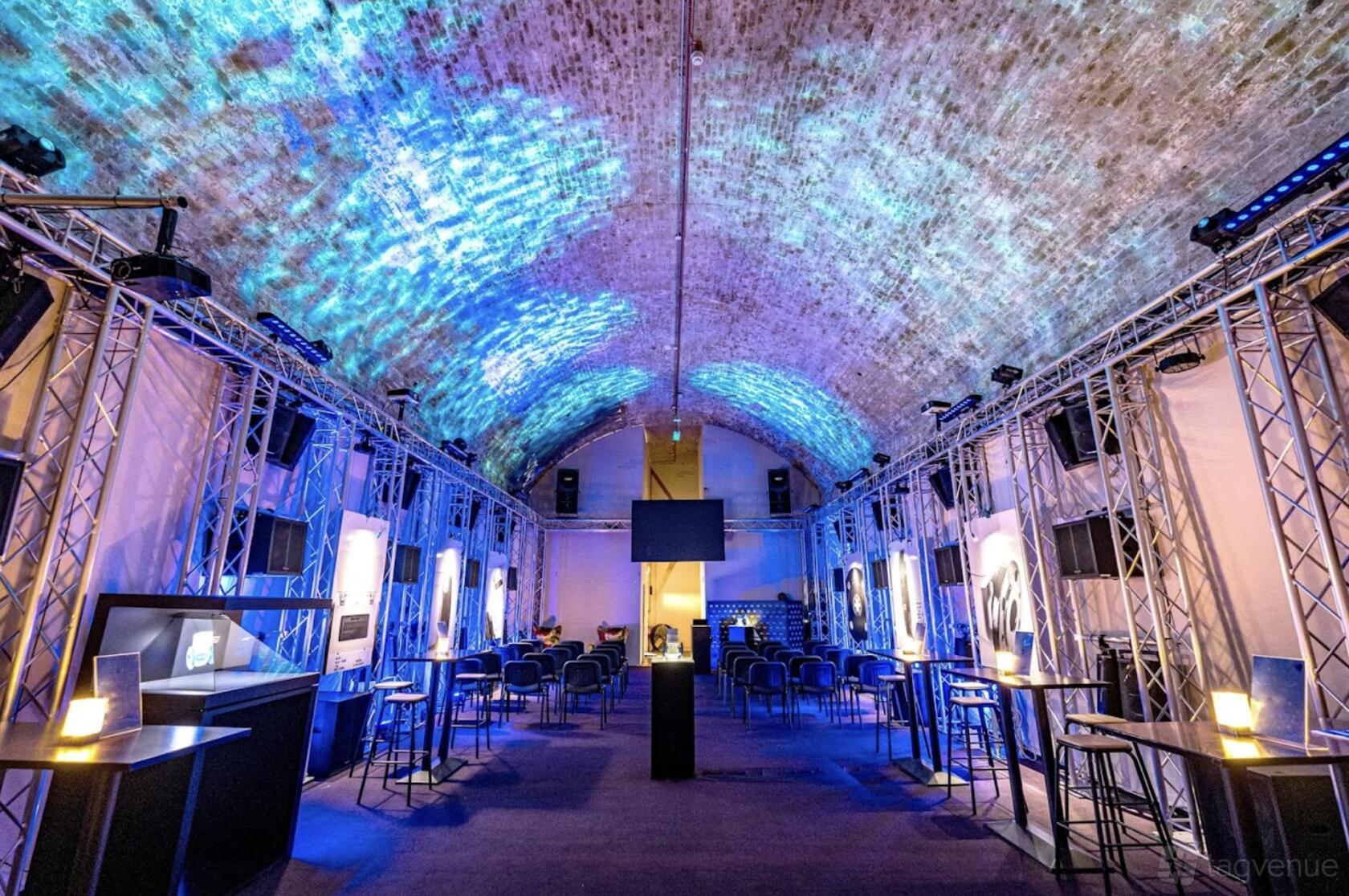 An event venue with arched exposed brick ceiling, blue lighting effects, and metal truss installations at Aures London.