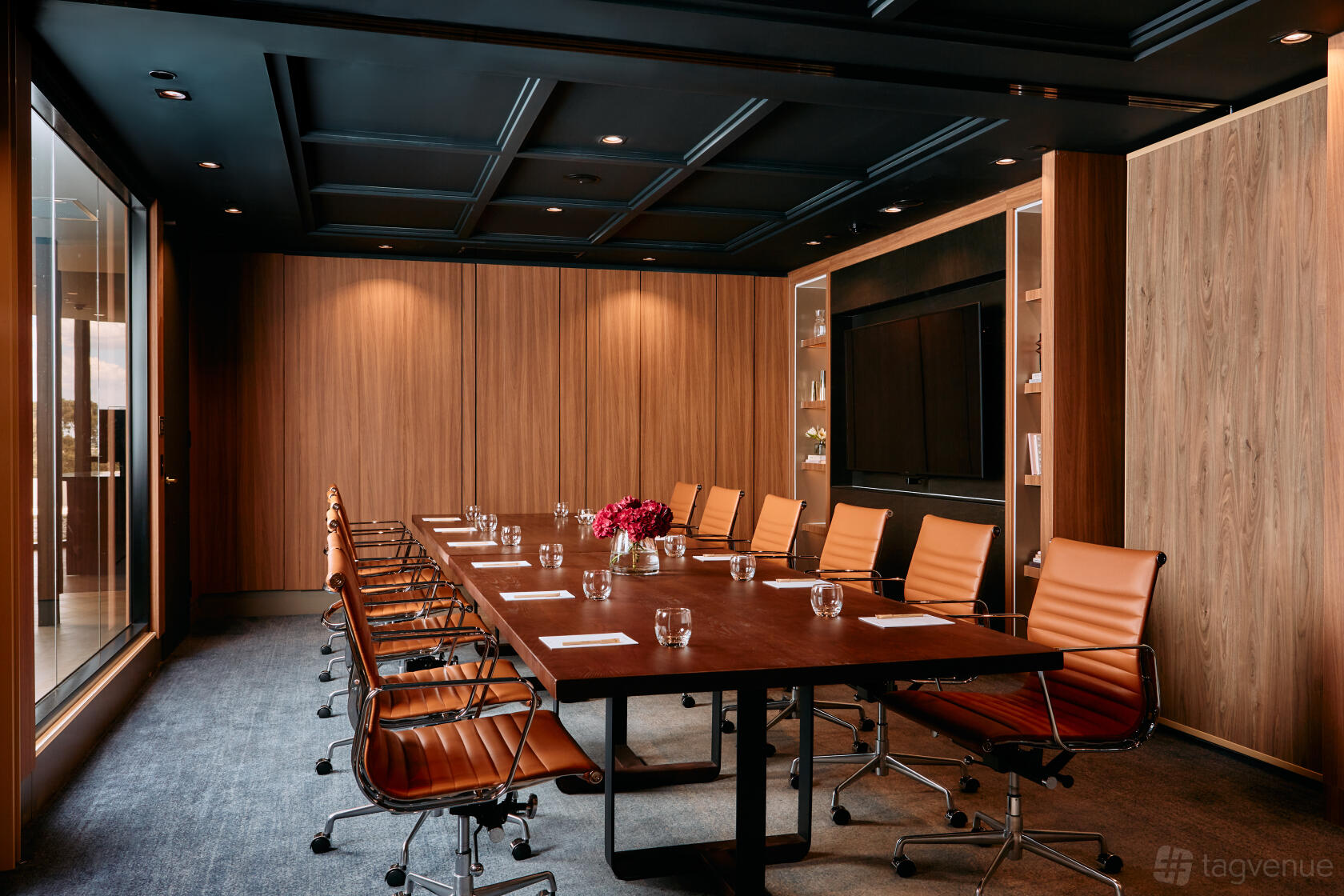 A boardroom with a long wooden table, tan leather chairs, wood panel walls, and a large screen at Mercure Melbourne Doncaster Tramway Room.