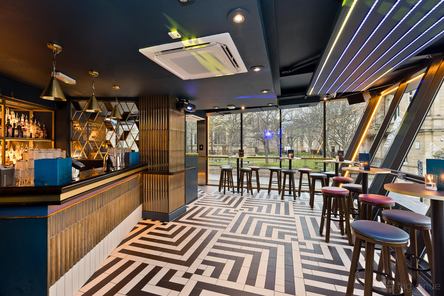 An event space in a cocktail bar with patterned tile flooring, floor-to-ceiling windows, and modern bar seating at Be At One Newcastle.