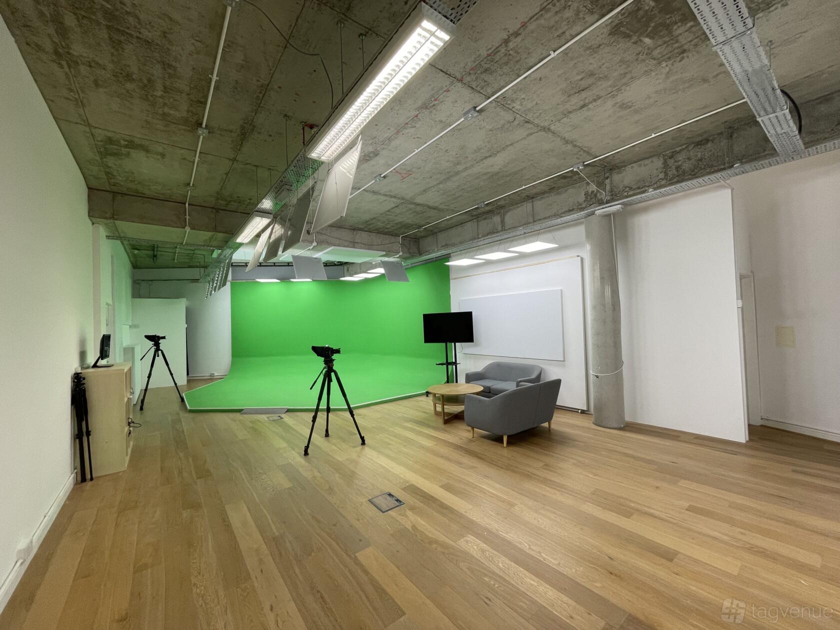 A recording studio with a green screen wall, wood flooring, and video cameras set up at TMH Studios.